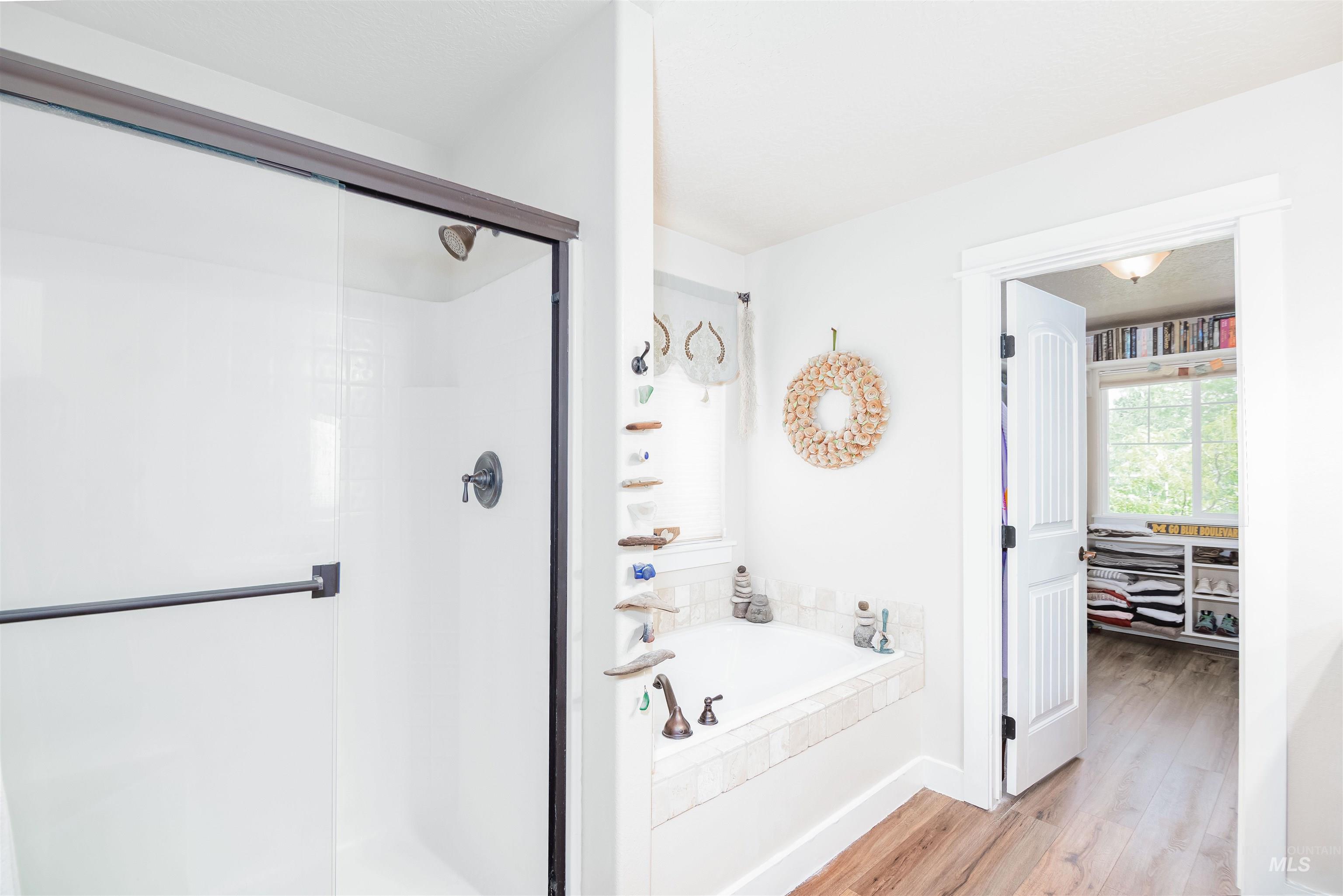 Bathroom featuring a walk-in shower with dark bronze framing and fixtures, a built-in soaking tub with tiled surround, and wood-finish flooring
