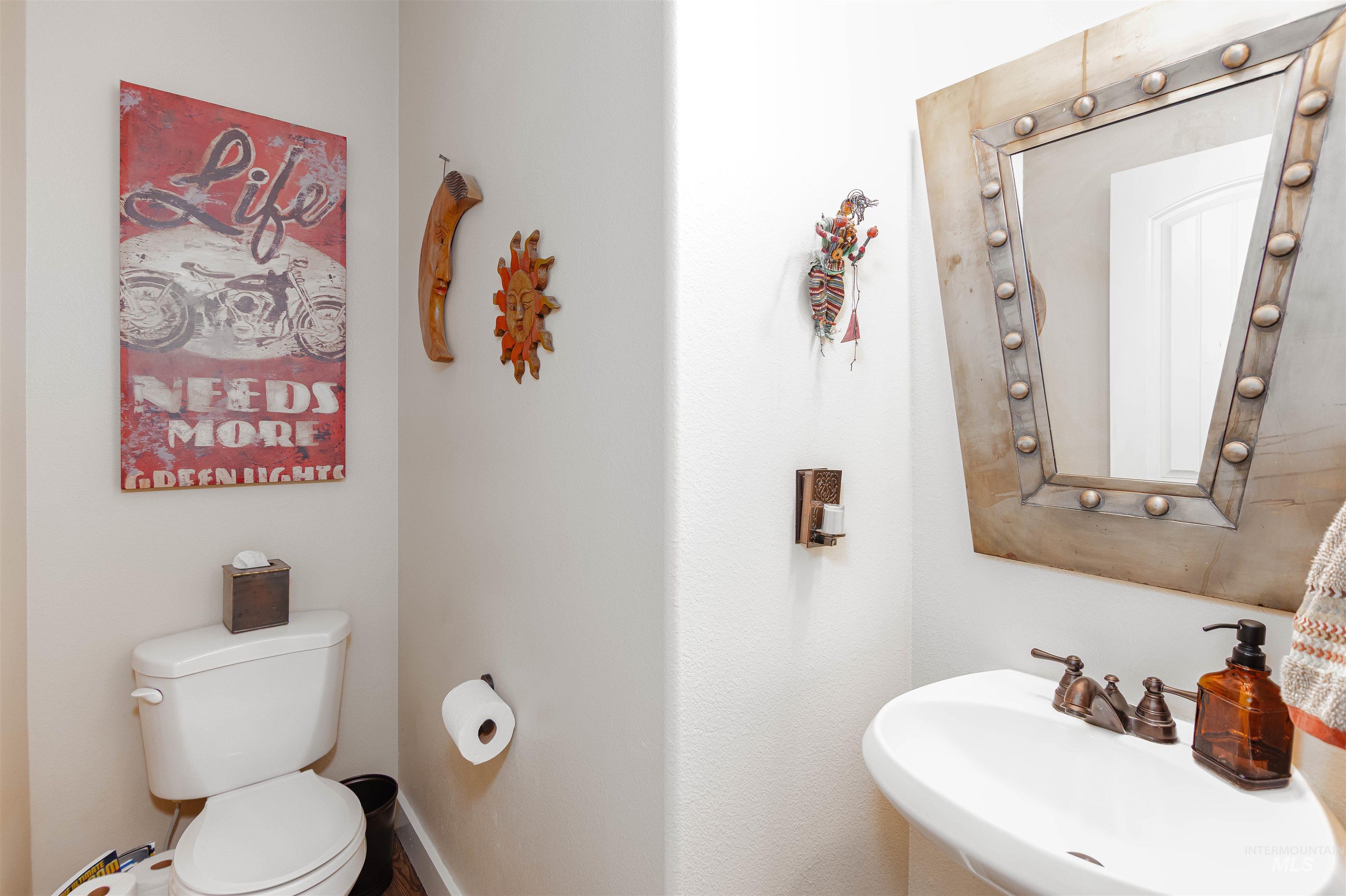 Powder room featuring a pedestal sink, a wall-mounted mirror with a studded frame, a two-piece toilet, and a brass-tone faucet