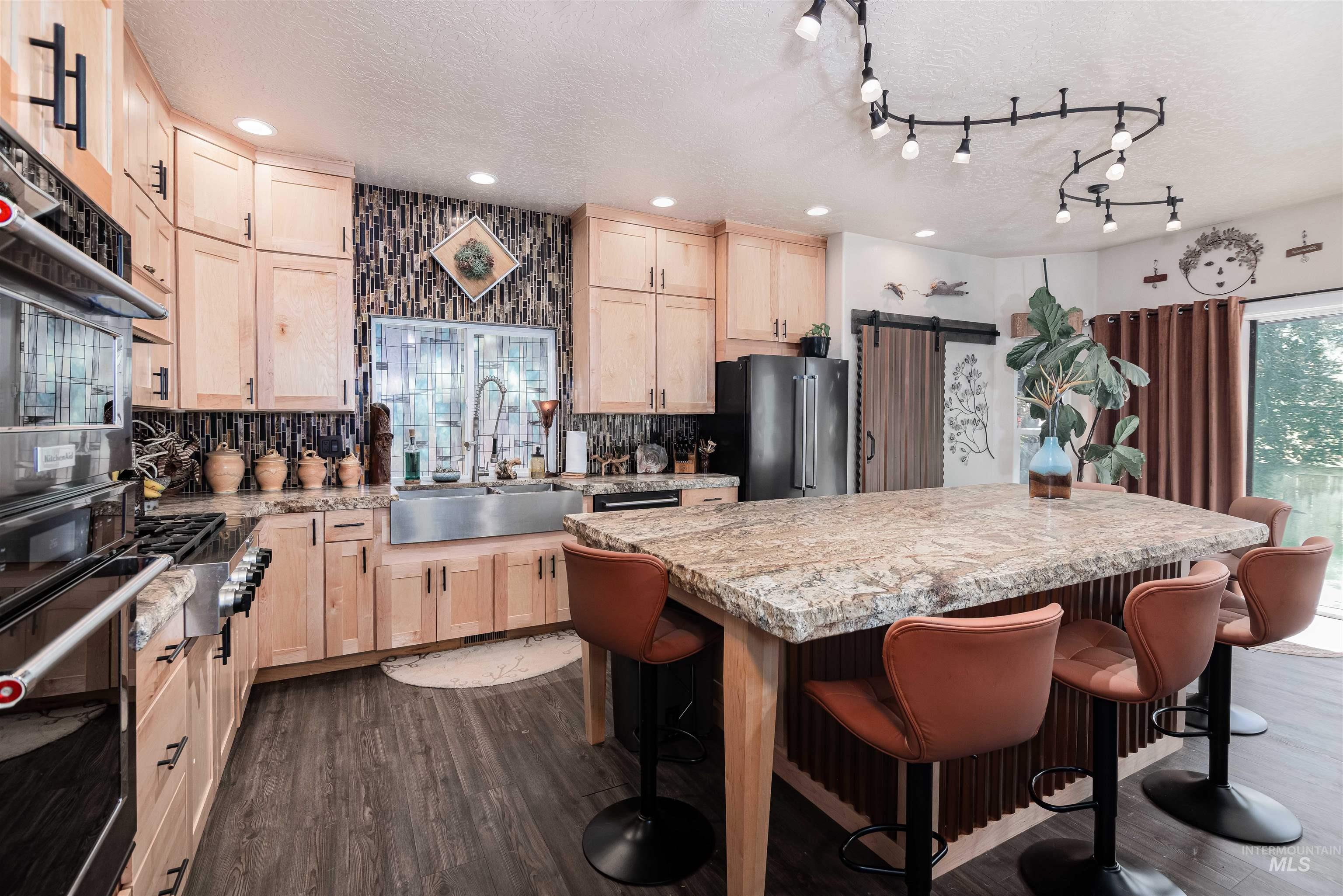 Kitchen featuring wood-finish flooring, light wood cabinetry, stone countertops, and a large central island