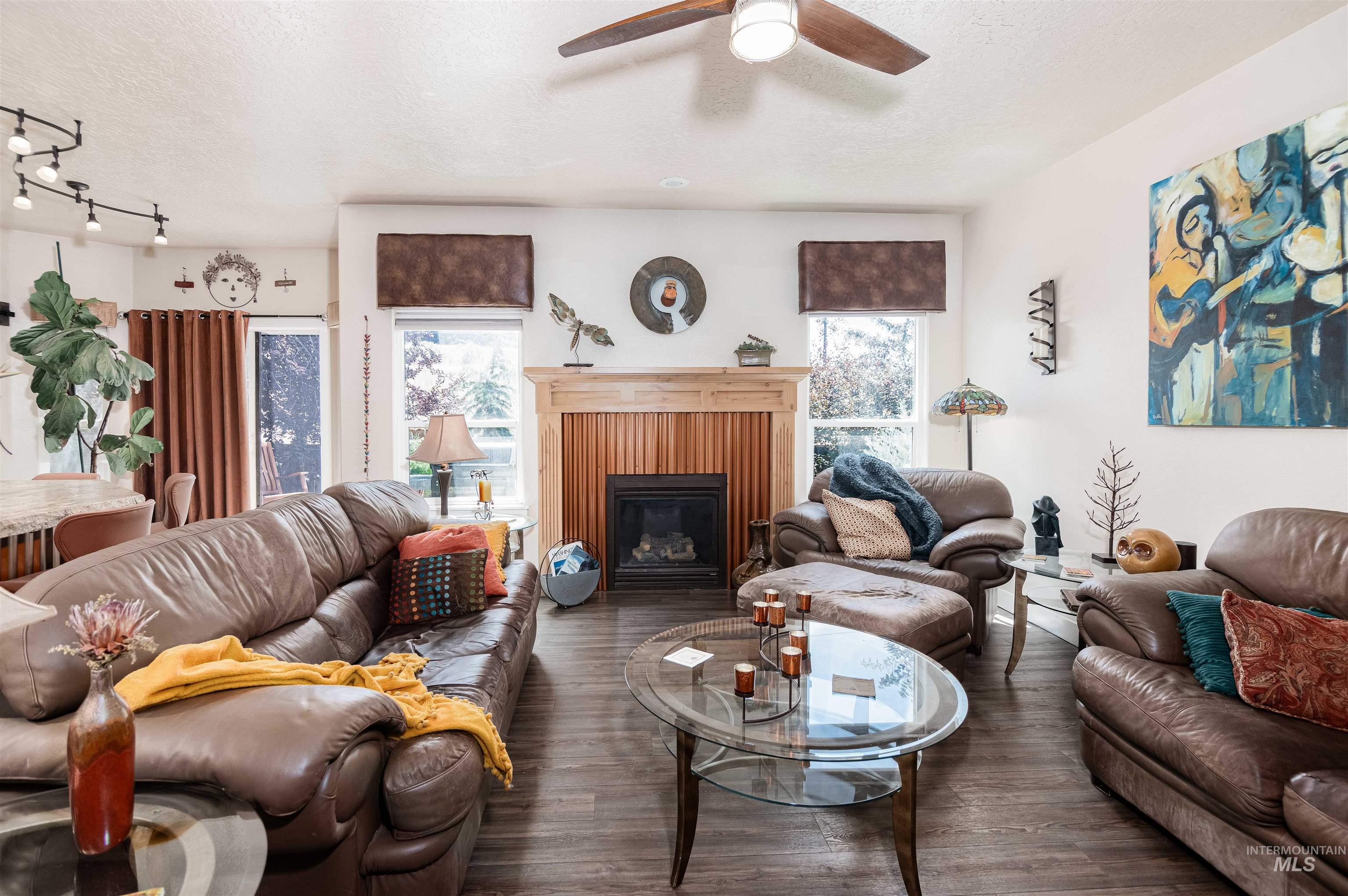 Living area featuring wood-finish flooring, a fireplace with a wood mantel and paneling, and a ceiling fan with integrated lighting
