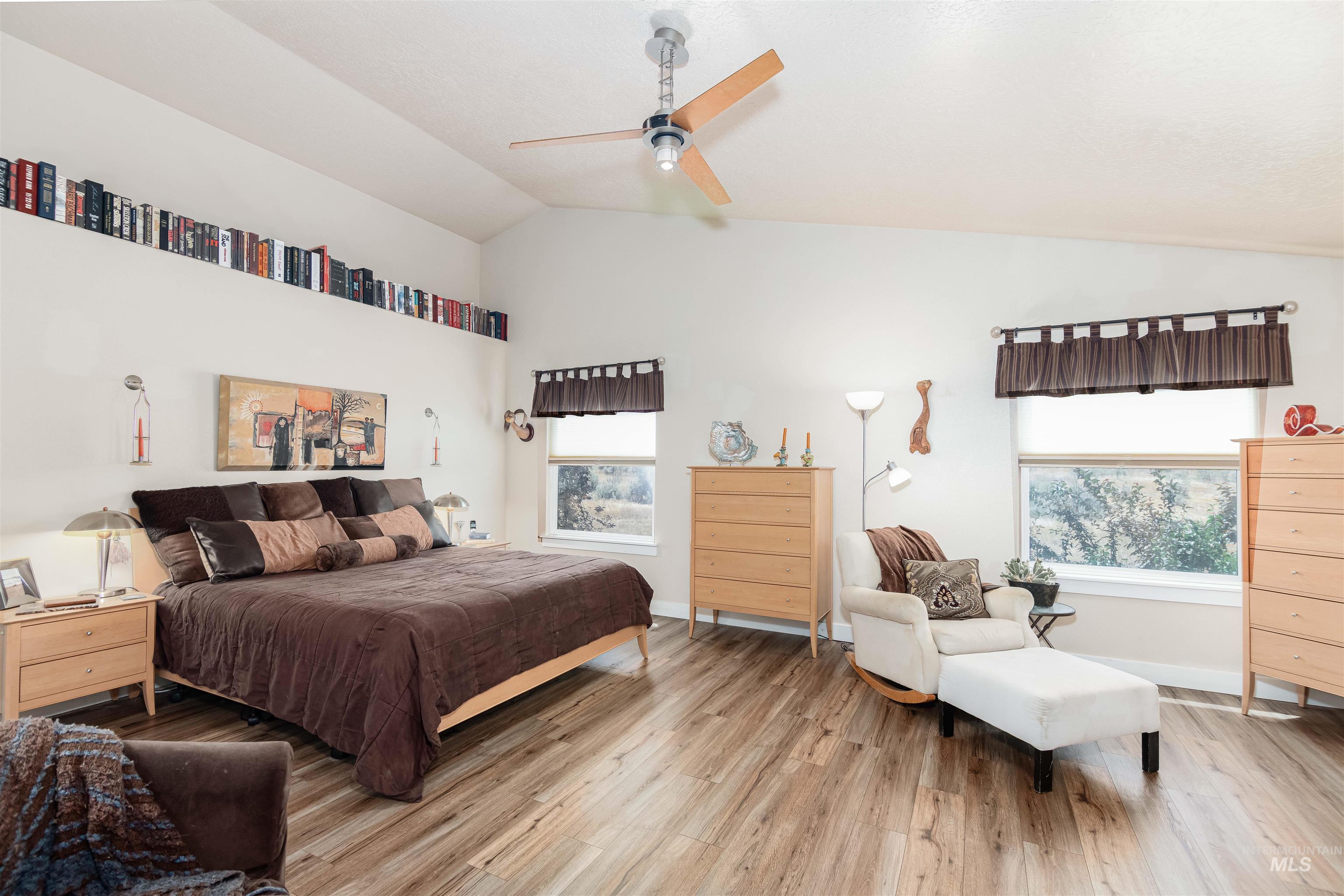 Vaulted ceiling bedroom featuring wood-finish flooring, recessed wall shelving, and dual windows