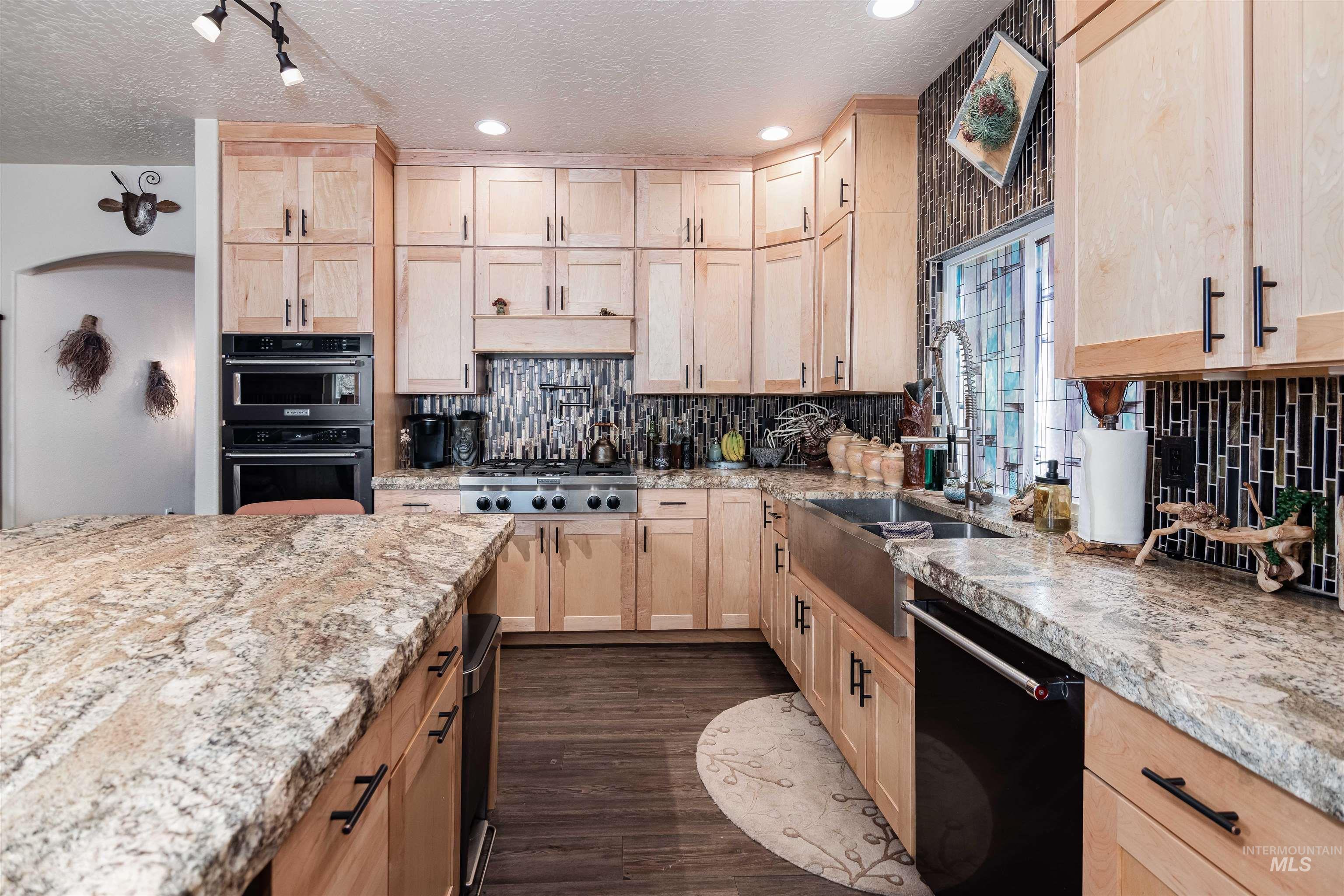 Gourmet kitchen featuring extensive light wood cabinetry, stone countertops, a stainless steel farm sink, double wall ovens, and a gas range