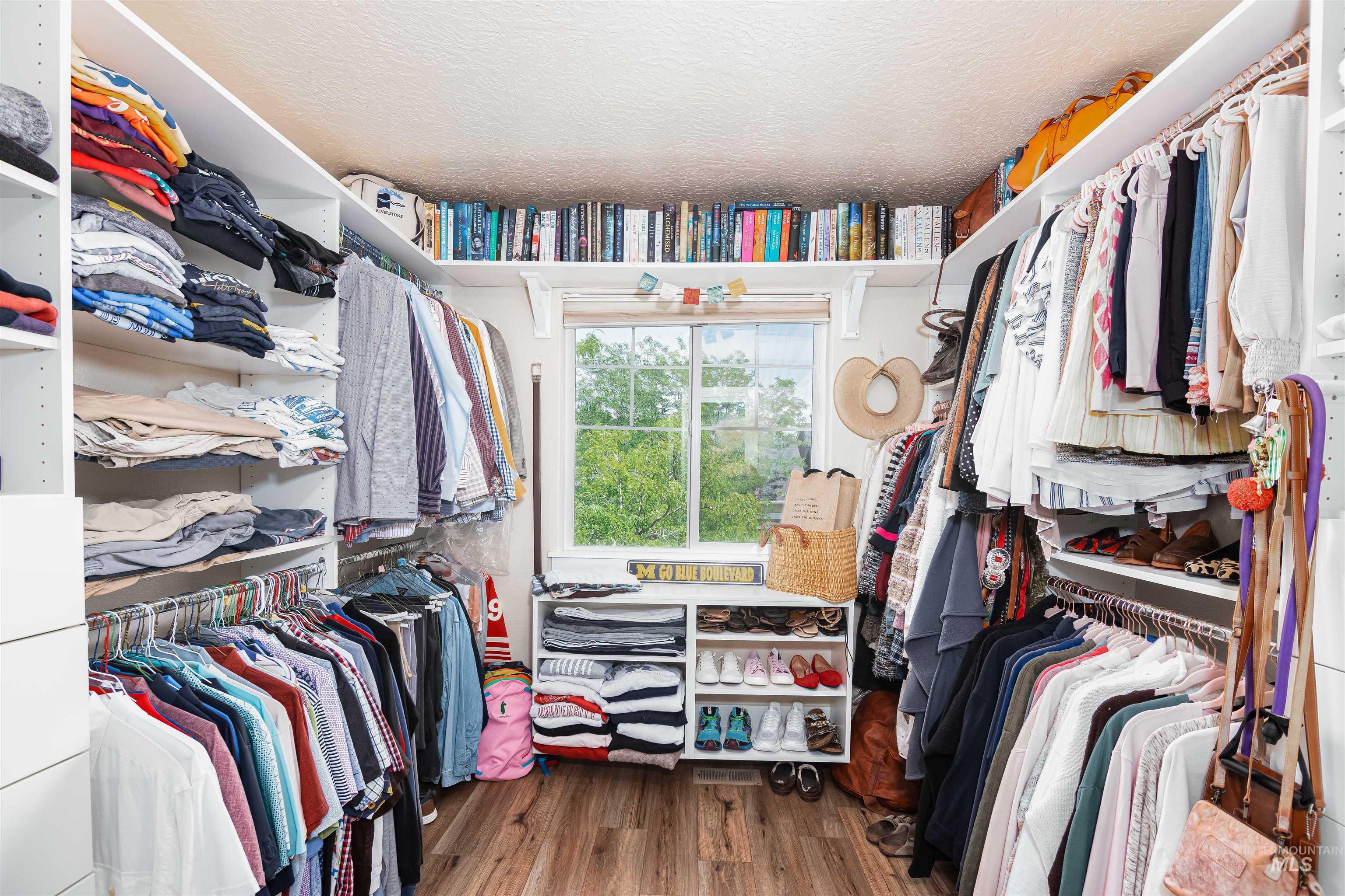 Walk-in closet featuring wood-finish flooring, a window offering natural light, built-in shelving, and multiple hanging rods for extensive storage