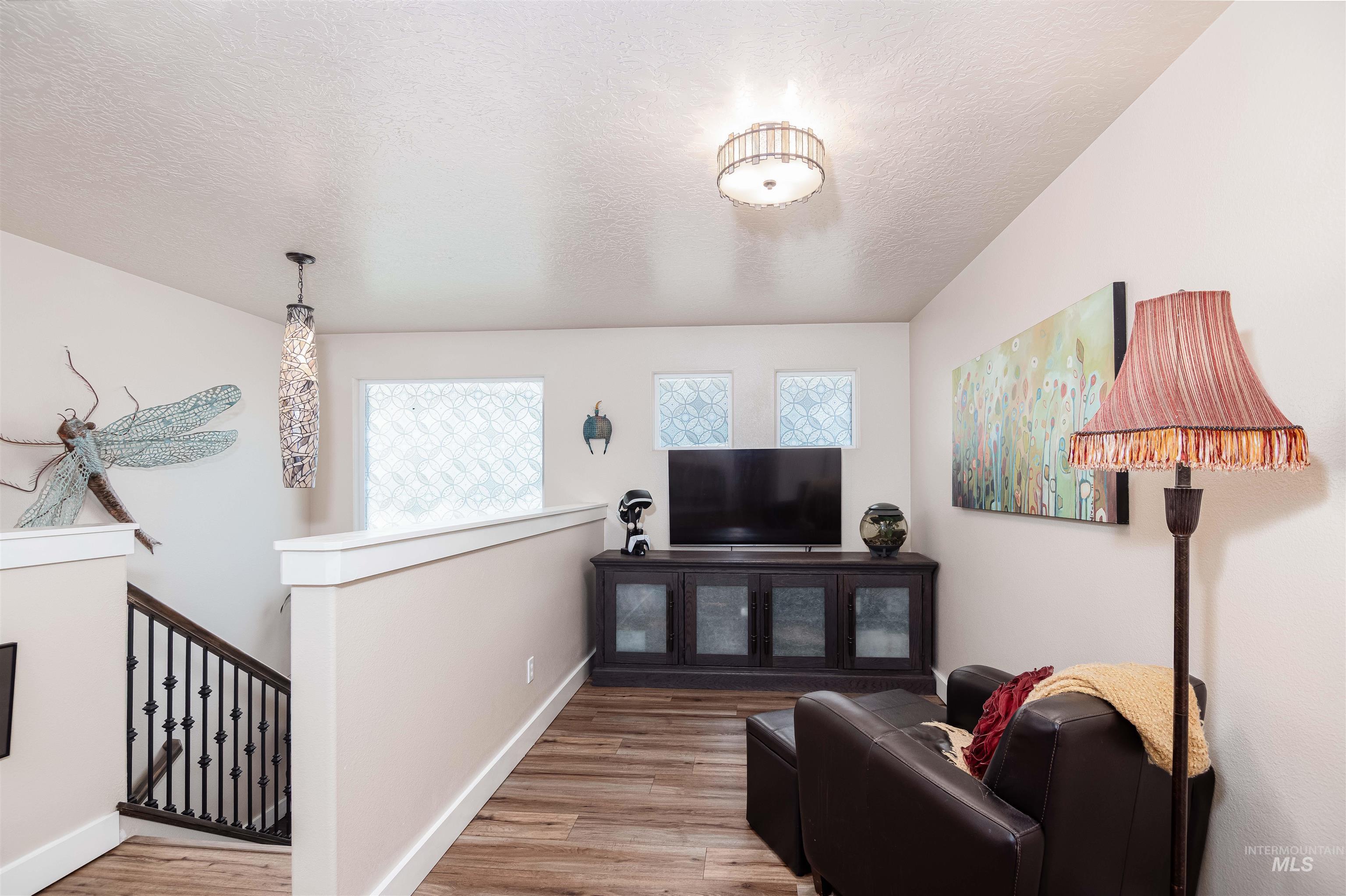 Spacious upper-level landing featuring wood-finish flooring, a contemporary lighting, and a staircase with wrought iron balusters