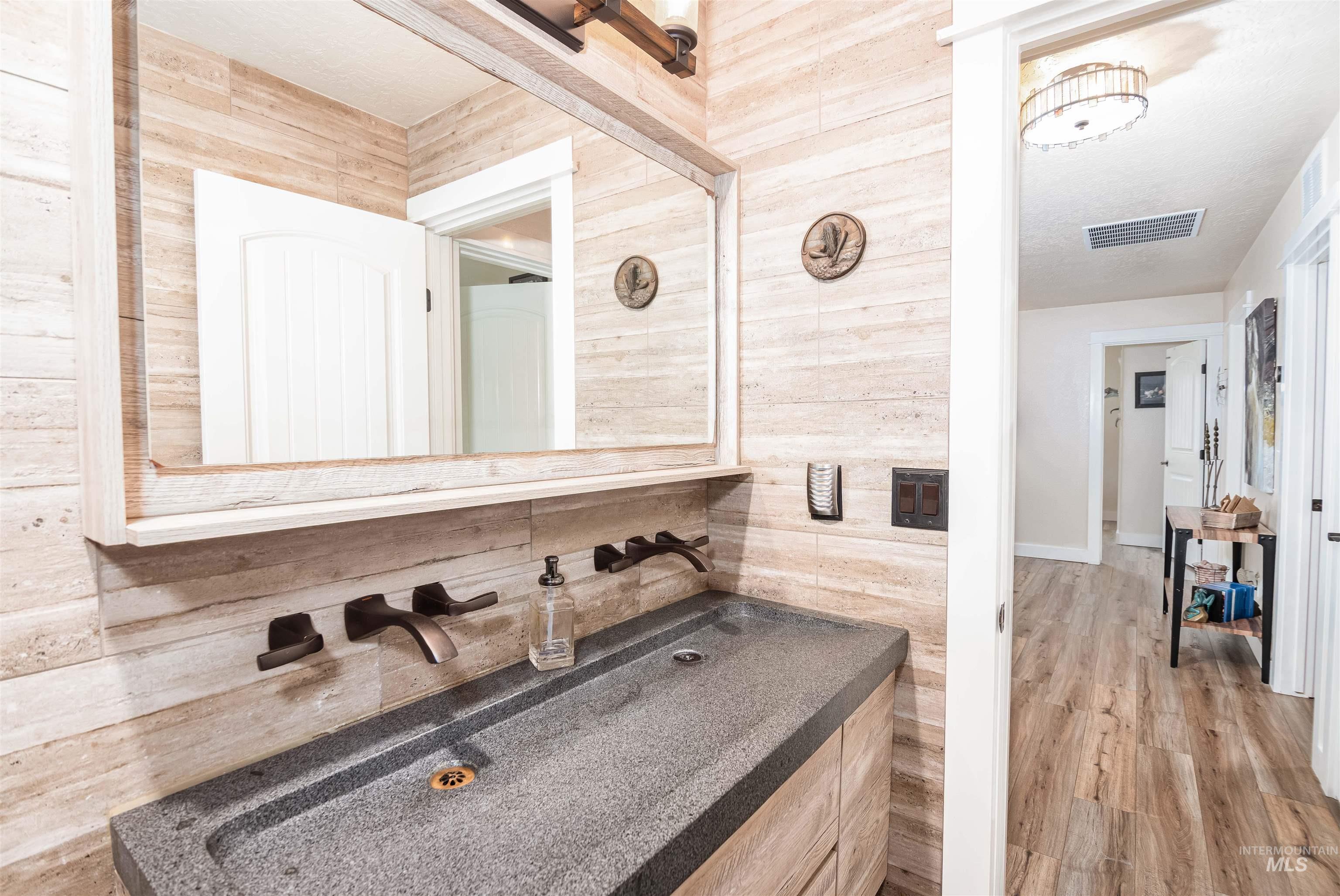 Bathroom vanity featuring a textured stone countertop with an integrated basin, wall-mounted bronze-finish faucets, and wood-finish wall paneling