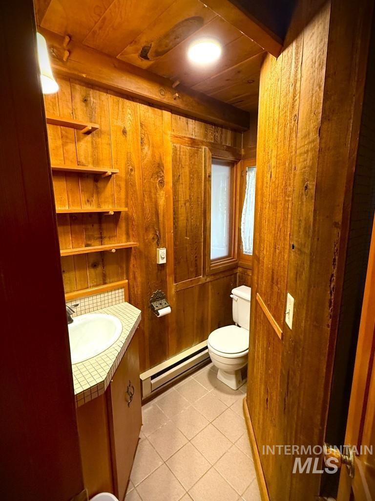 Half bathroom featuring a baseboard radiator, vanity, tile patterned flooring, wooden walls, and wood ceiling