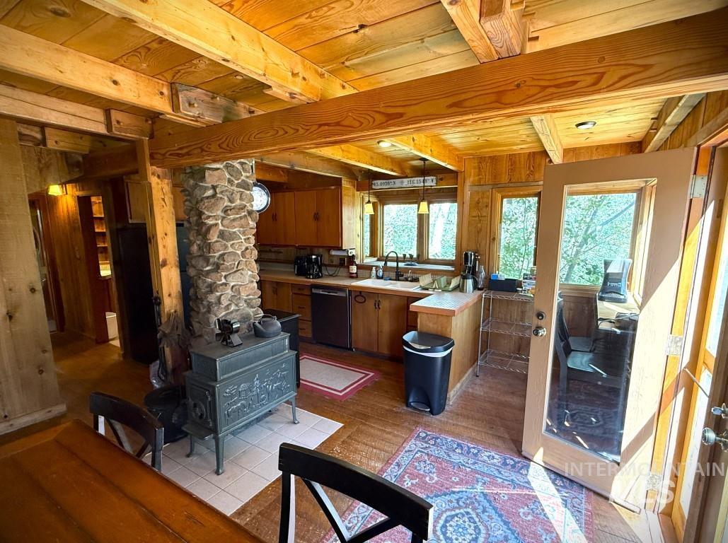 Kitchen with a wood stove, black dishwasher, light countertops, wooden walls, and brown cabinets