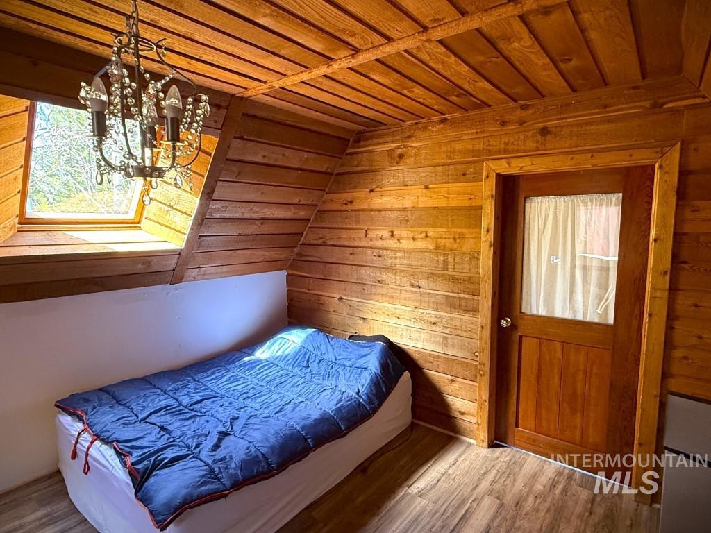 Bedroom featuring wooden walls, wood ceiling, wood finished floors, and a chandelier