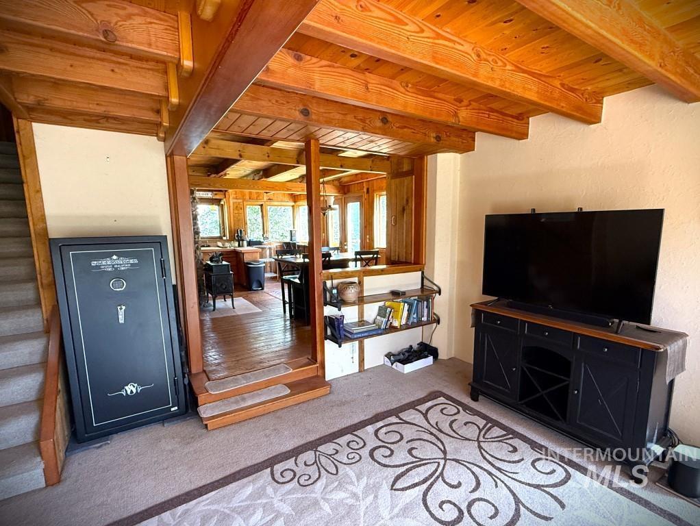 Carpeted living area with stairs and a wooden ceiling with exposed beams