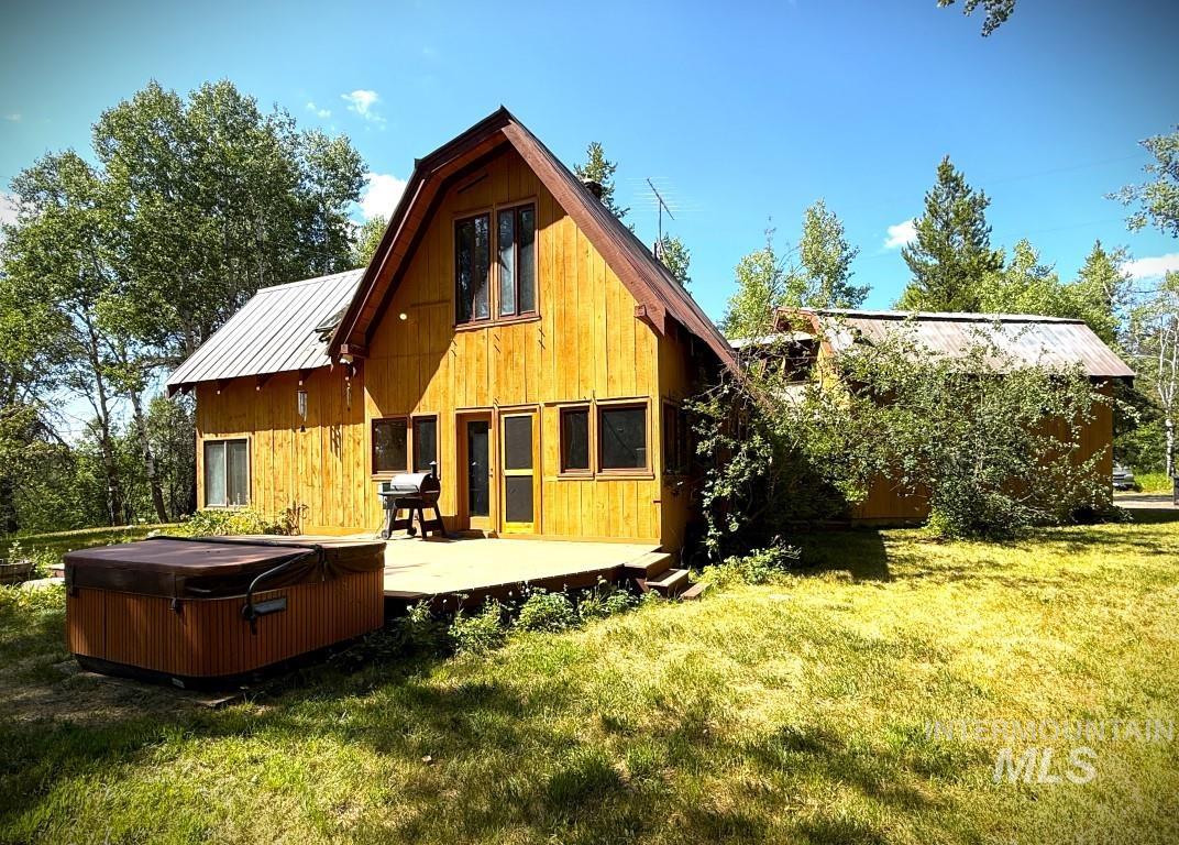 Back of house with a hot tub, a metal roof, a lawn, and a standing seam roof