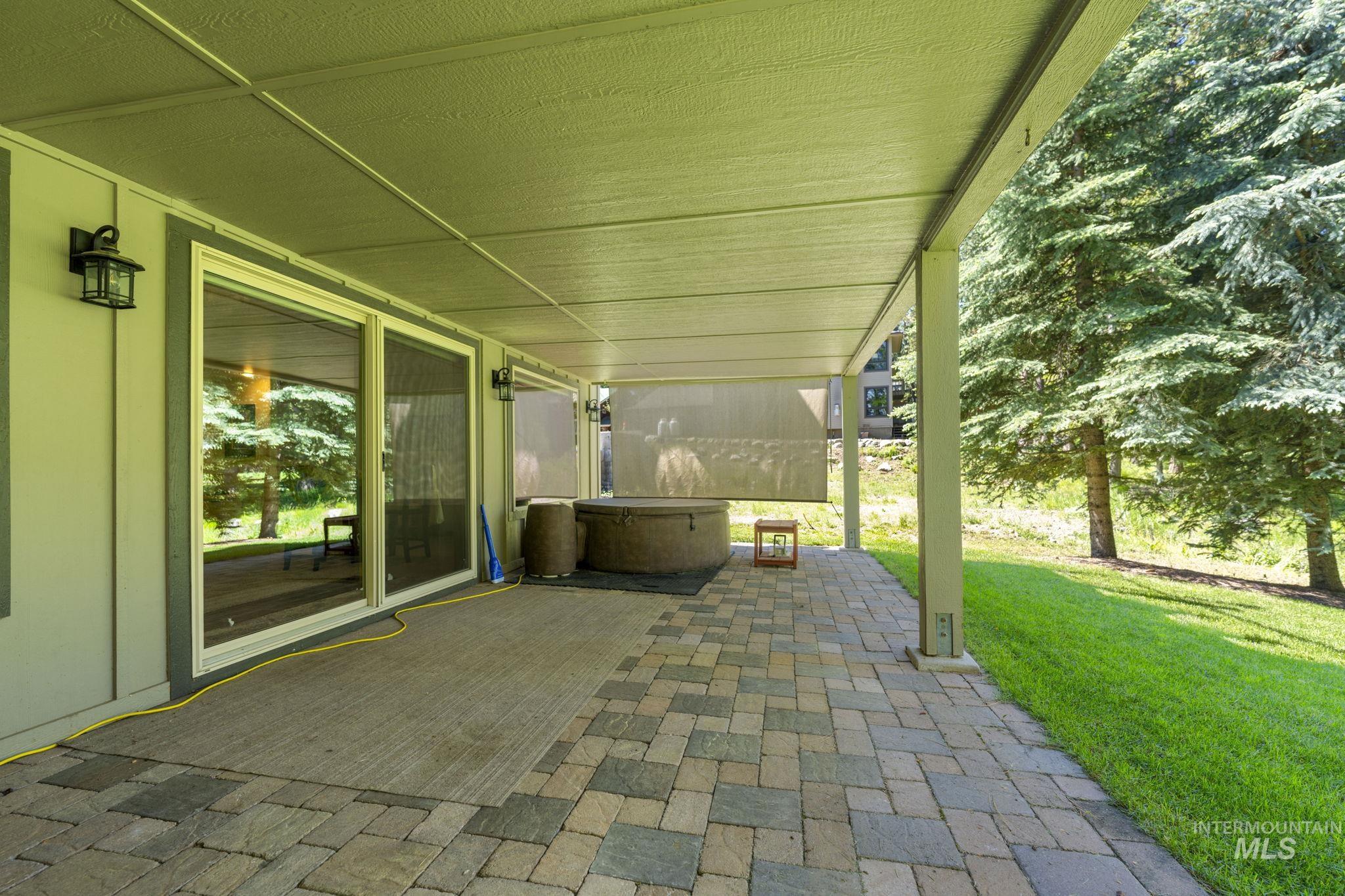 Expansive covered patio featuring multi-toned paver flooring, overhead lighting, and dual sliding glass doors