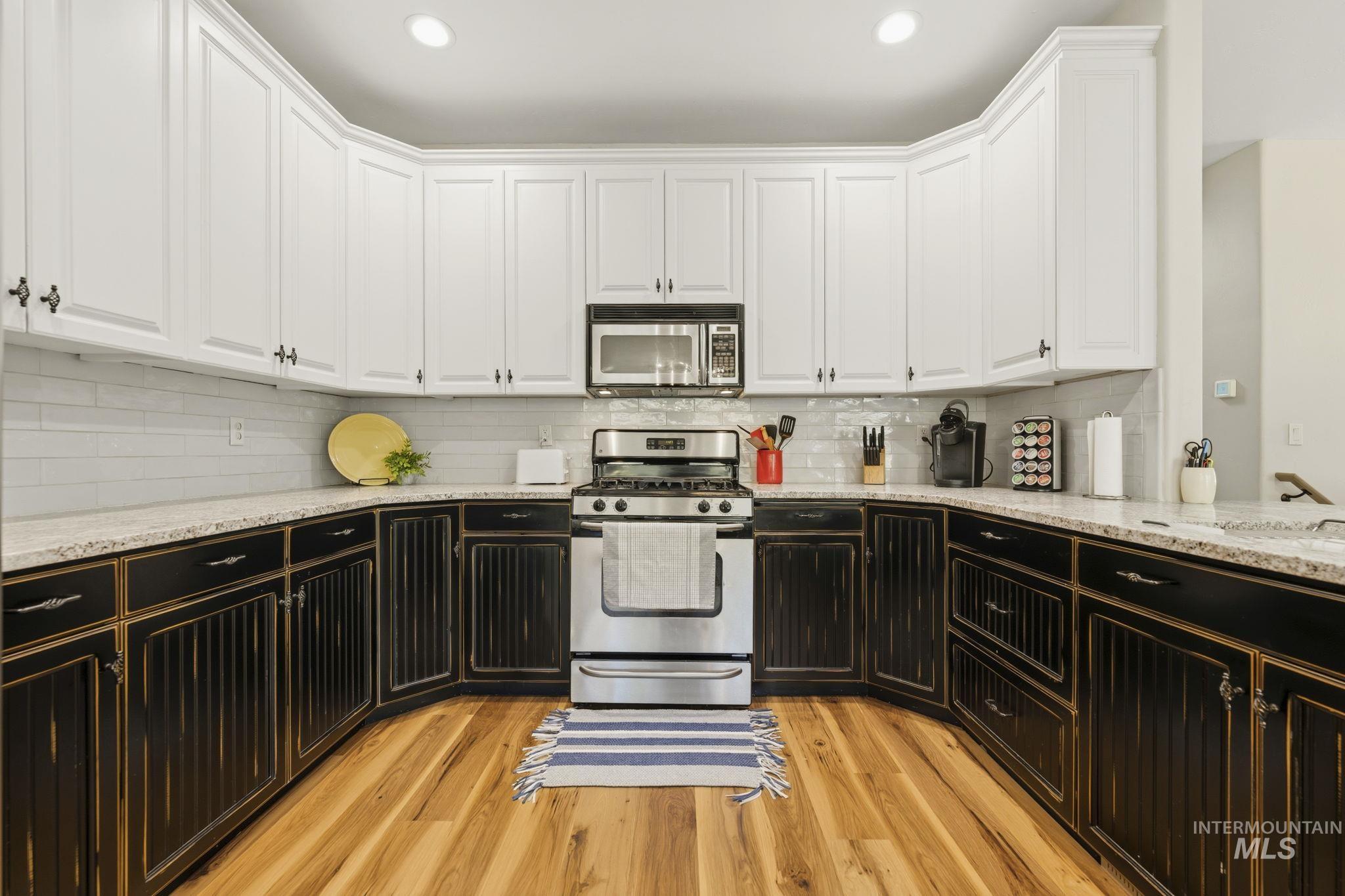 U-shaped kitchen featuring white upper cabinetry, distressed black lower cabinetry, stainless steel appliances, and wood-finish flooring