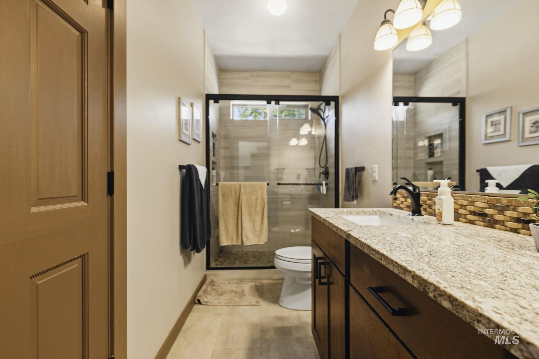 Bathroom featuring a spacious walk-in shower with a glass enclosure, a vanity with a light-toned countertop, a rectangular sink, a black faucet, and a large mirror