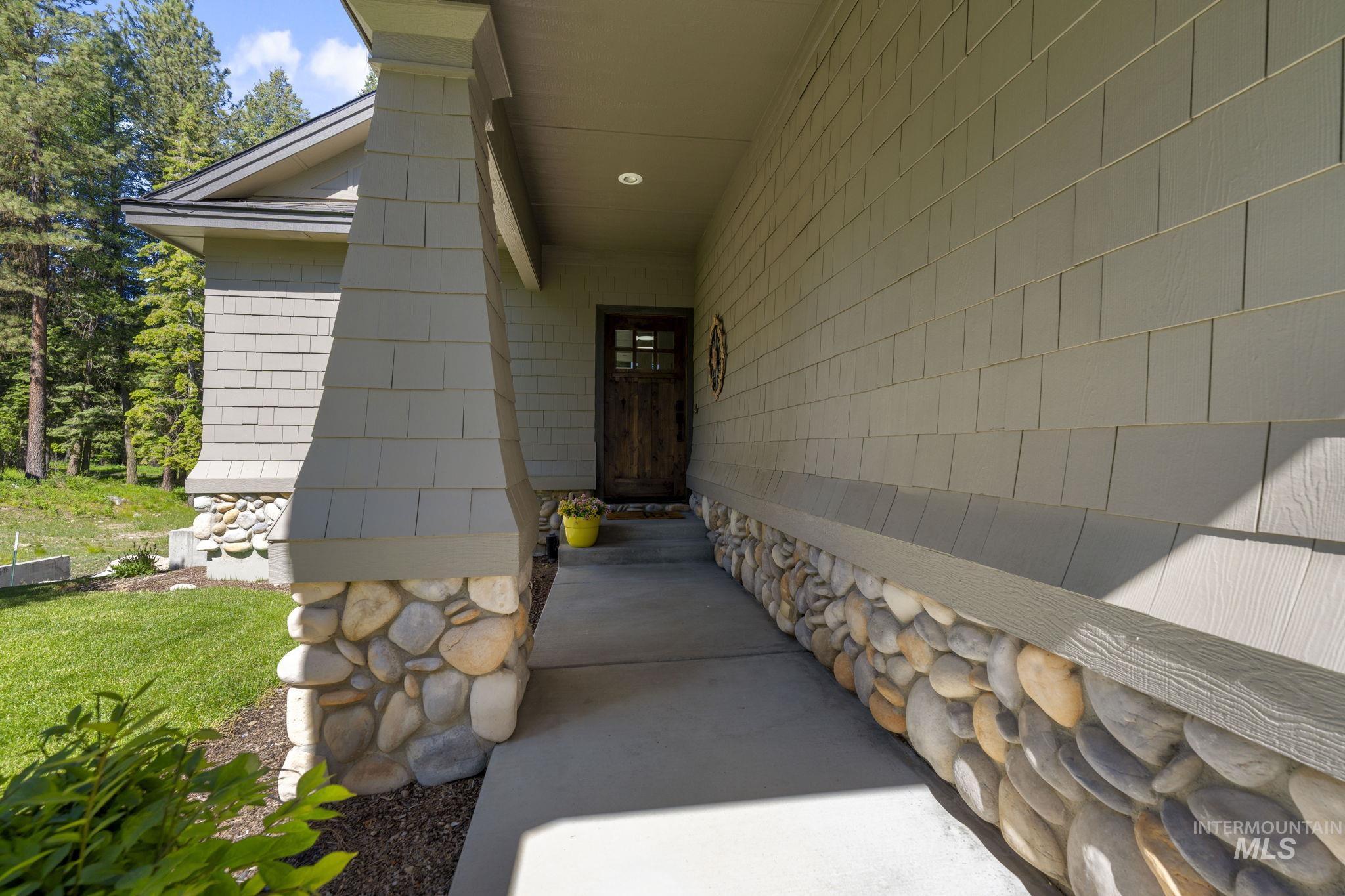 Front exterior featuring shake siding, a natural wood-finish entry door with glass panels, and river rock accents on the foundation and column base