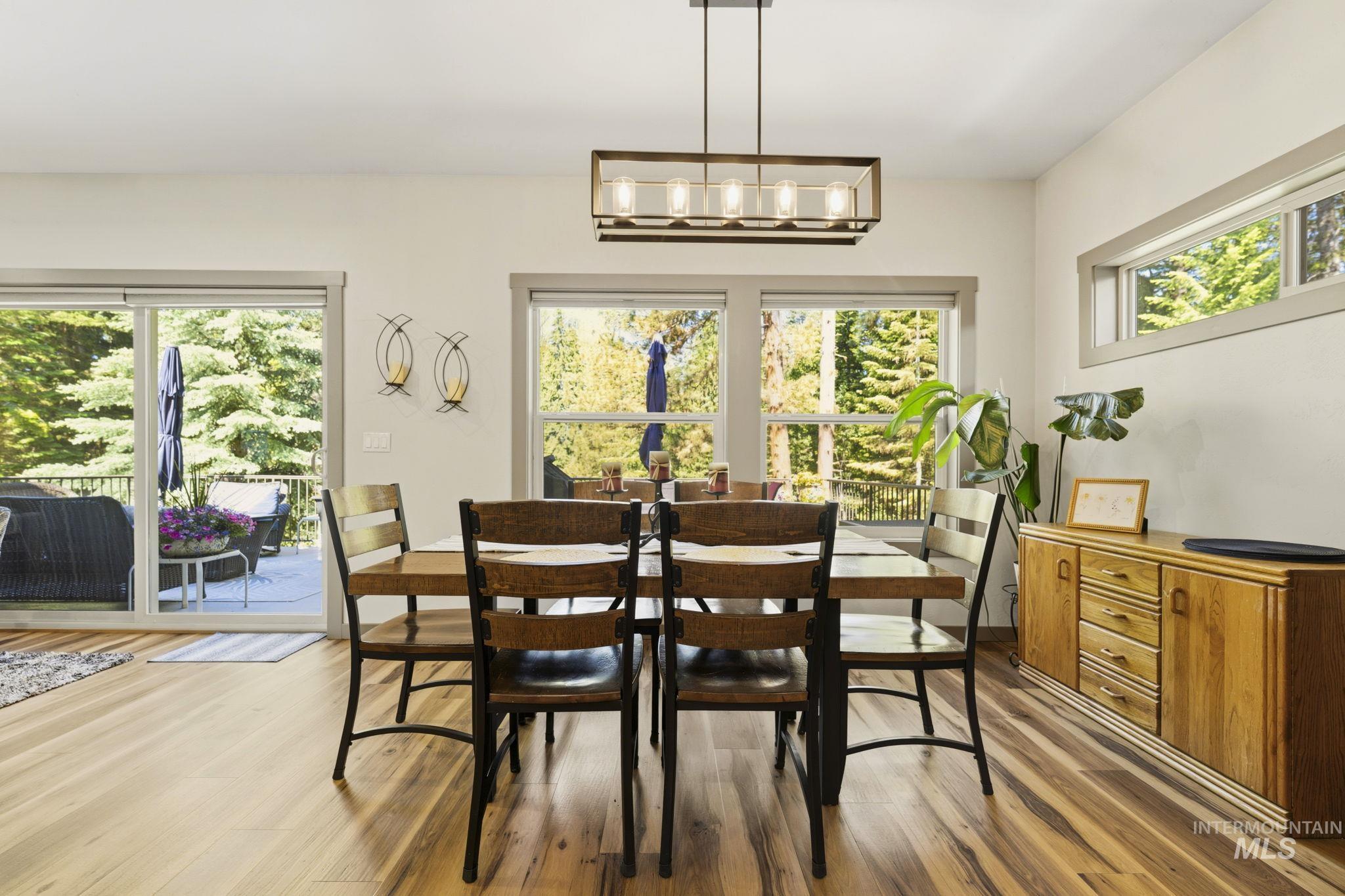 Dining area featuring wood-finish flooring, a linear chandelier, built-in horizontal windows, and sliding glass doors opening to an exterior deck