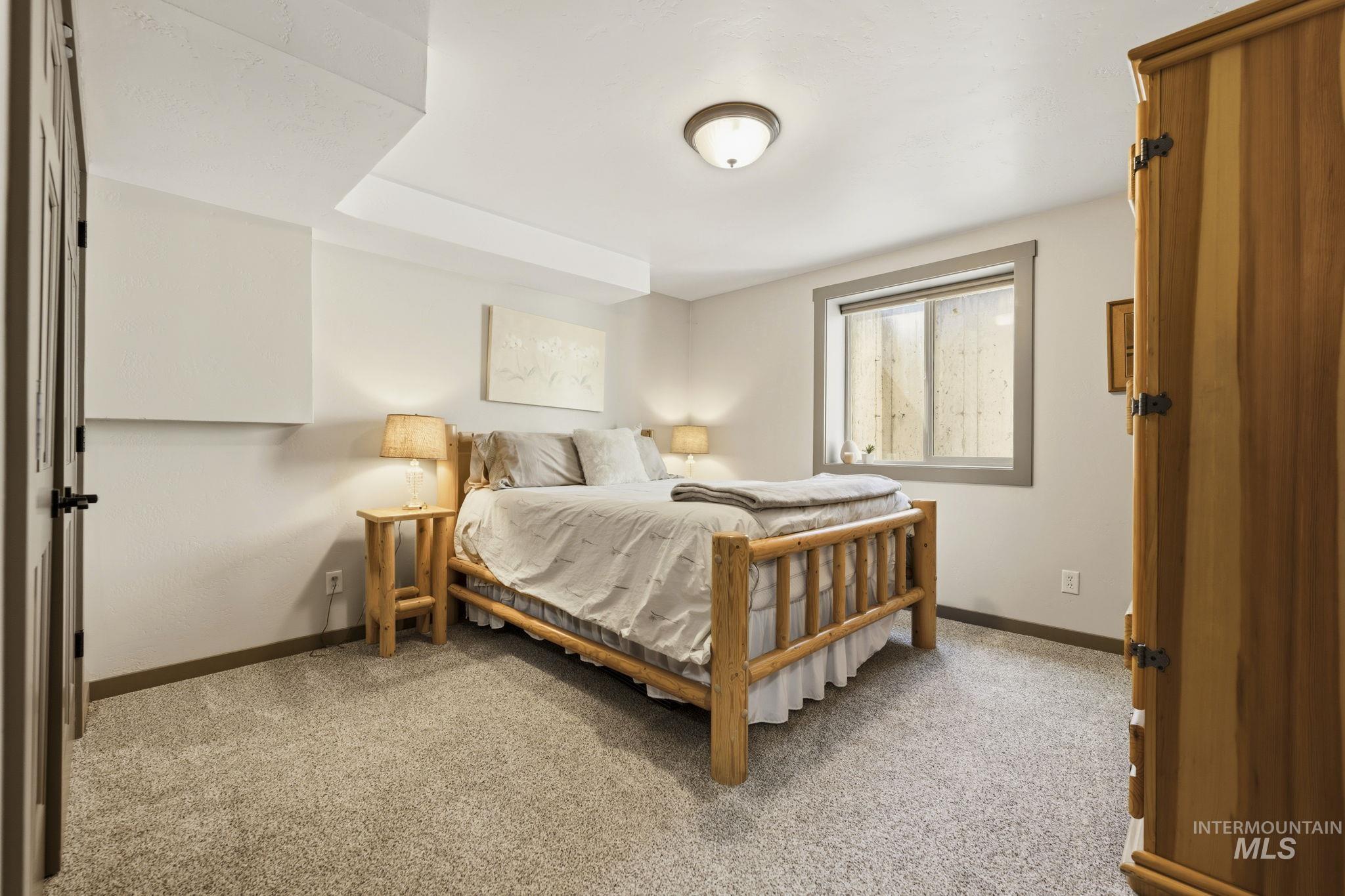 Carpeted bedroom featuring a transom window, warm gray walls, a ceiling-mounted light fixture, and a paneled door with dark hardware