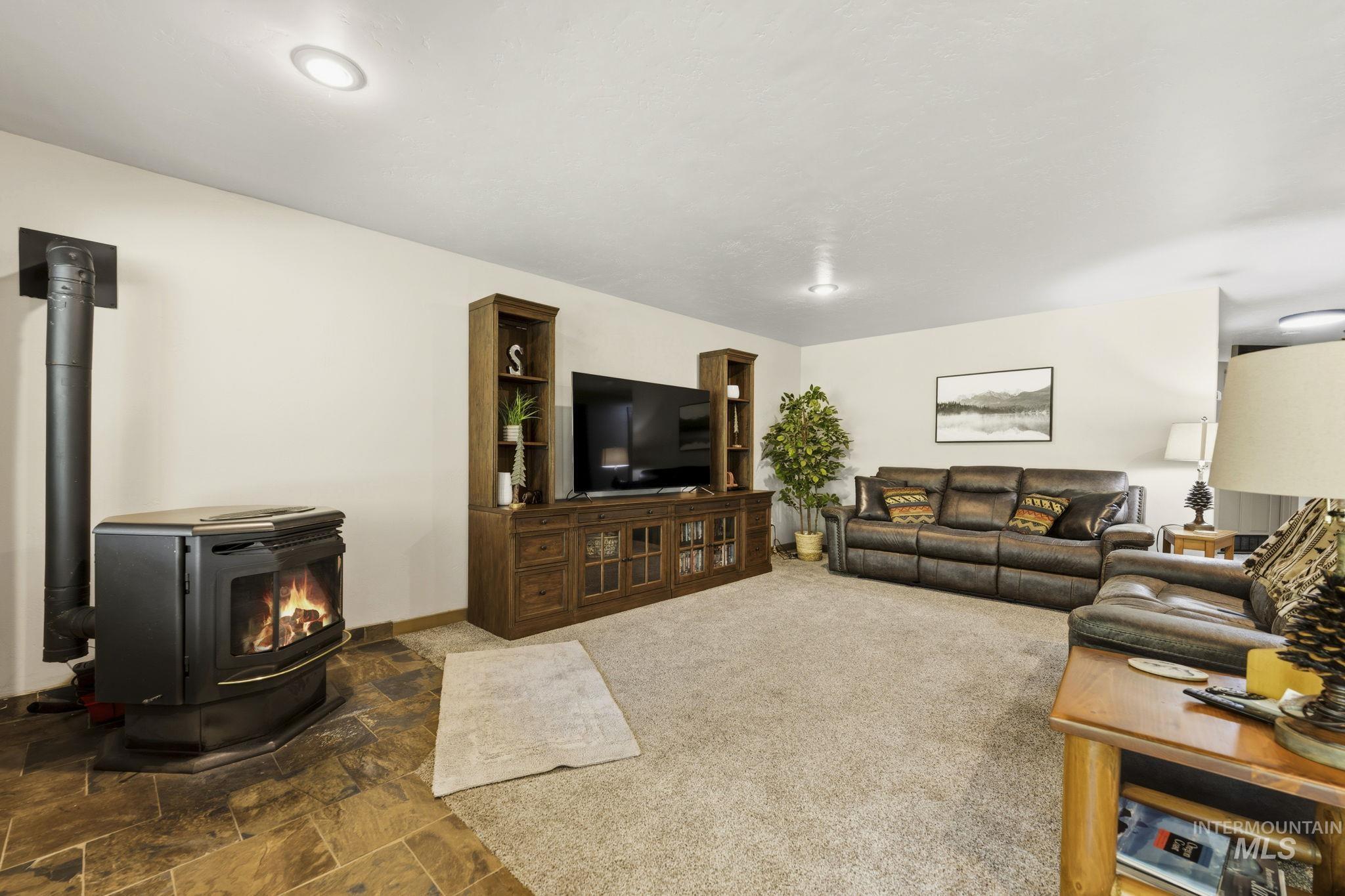 Inviting living area featuring a freestanding stove with a black flue, recessed lighting, and mixed flooring with carpet and natural stone-finish tiles
