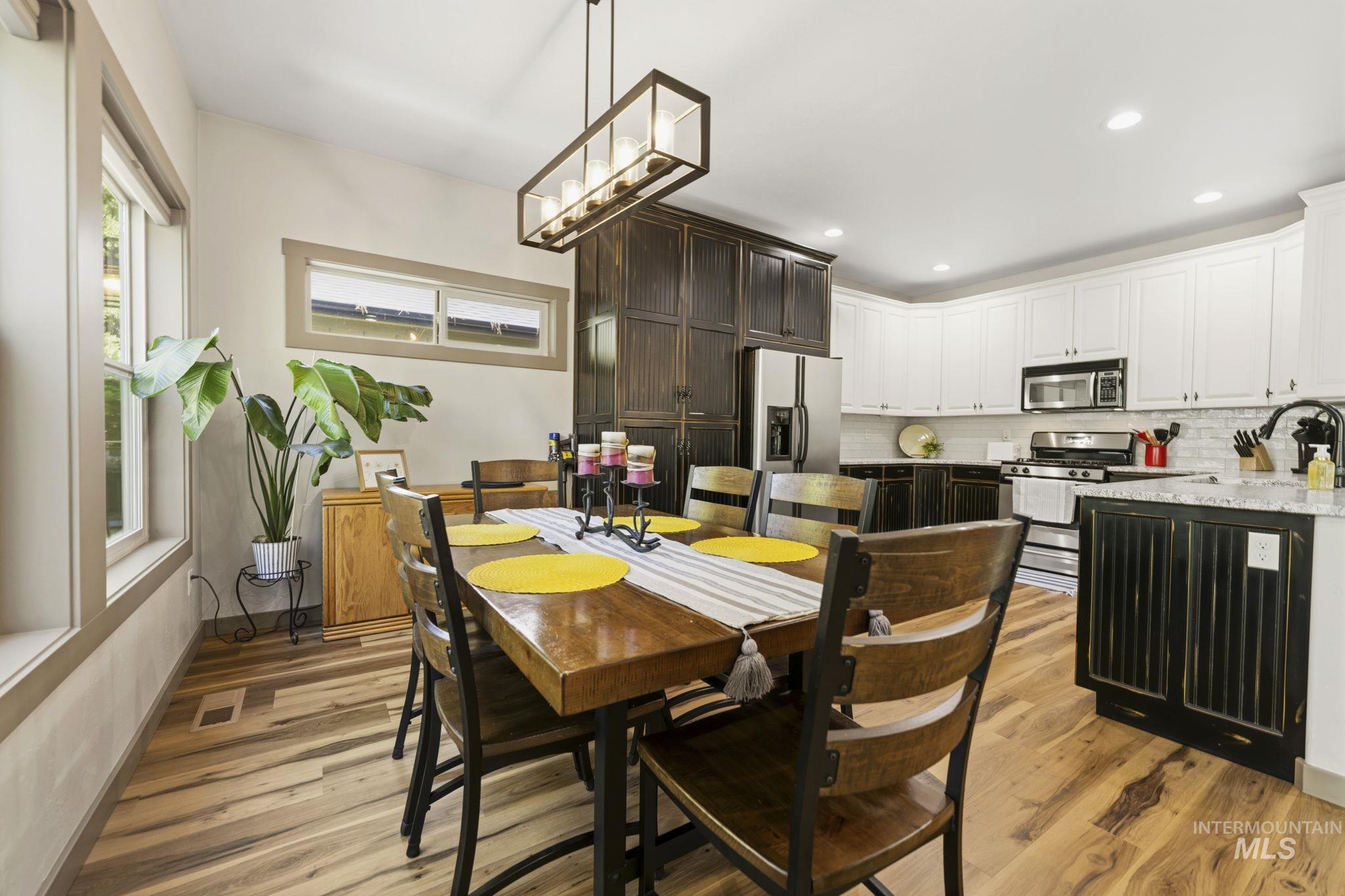 Open-concept dining area featuring wood-finish flooring, a linear chandelier, and ample natural light from multiple windows