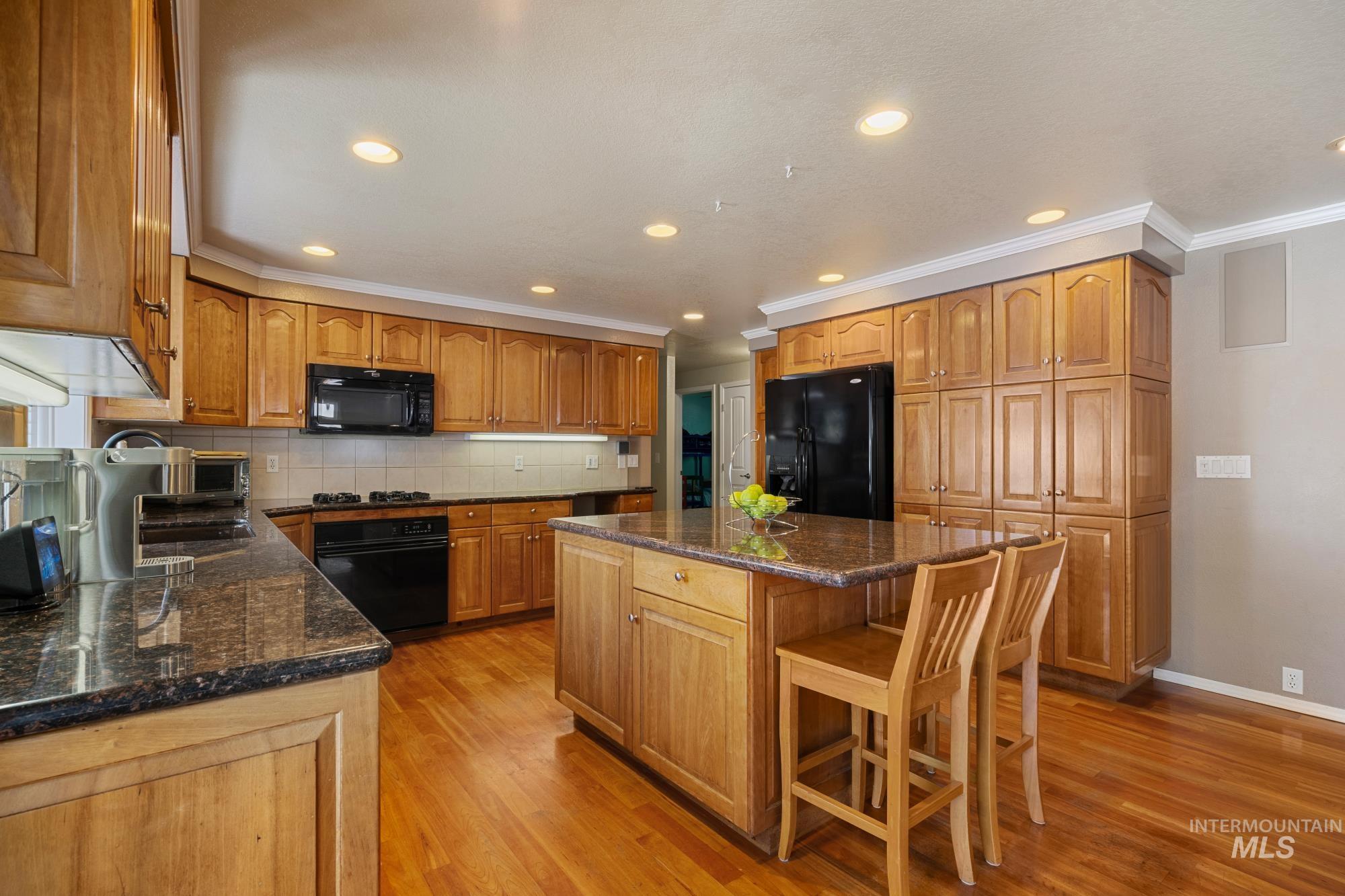 Kitchen with decorative backsplash, black appliances, recessed lighting, a kitchen island, and dark stone countertops