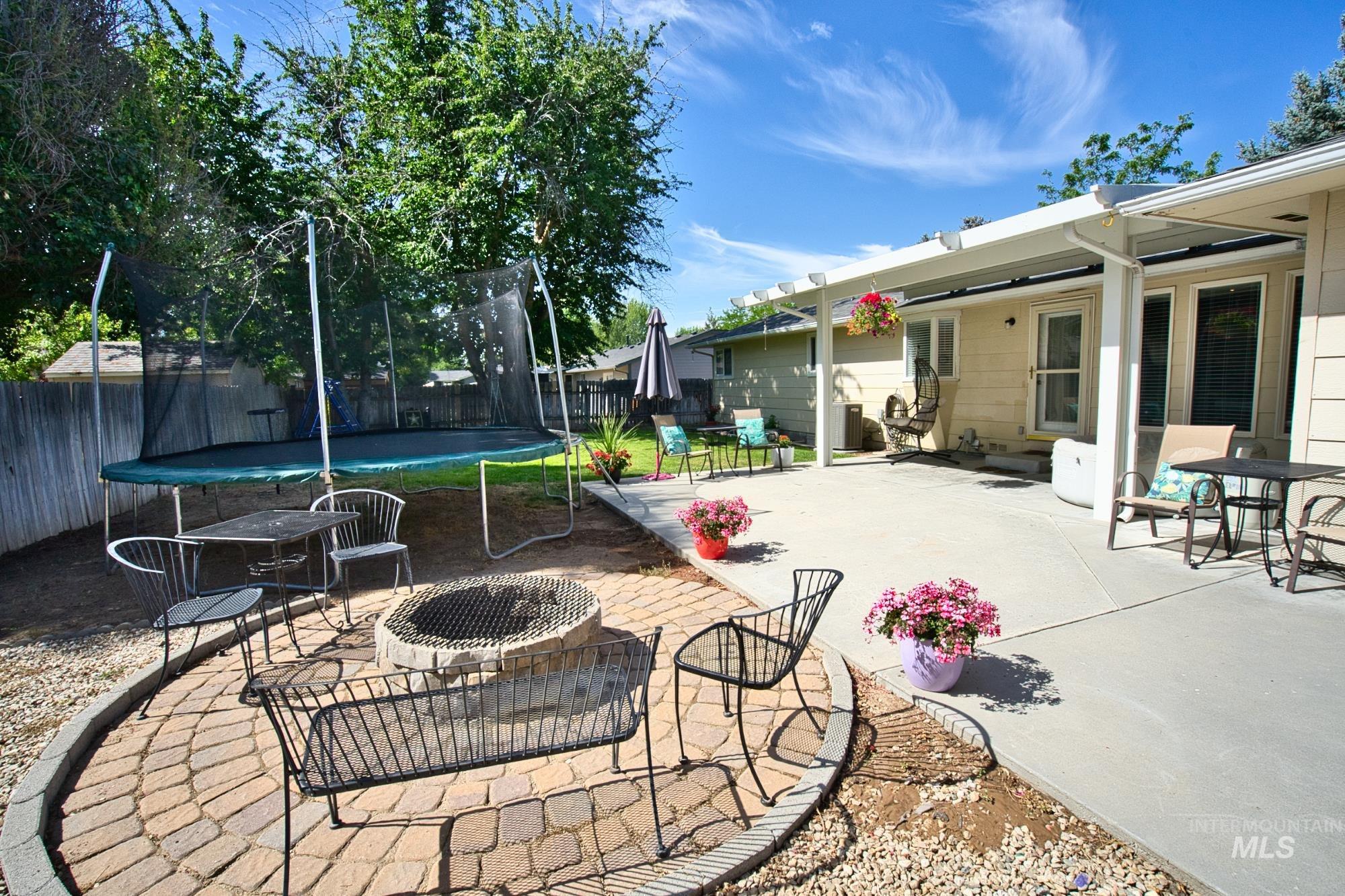 Fenced backyard featuring a trampoline, a patio, and a fire pit