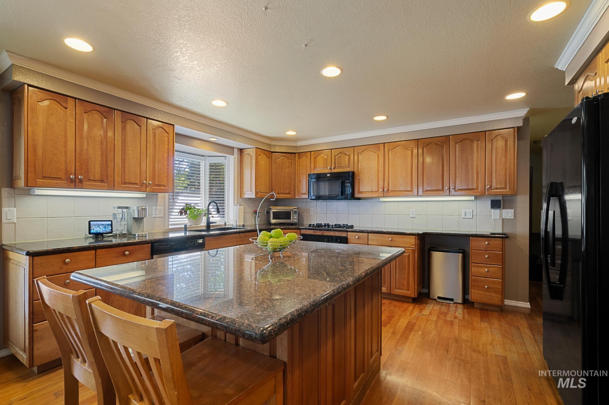 Kitchen featuring recessed lighting, backsplash, light wood finished floors, brown cabinetry, and black appliances