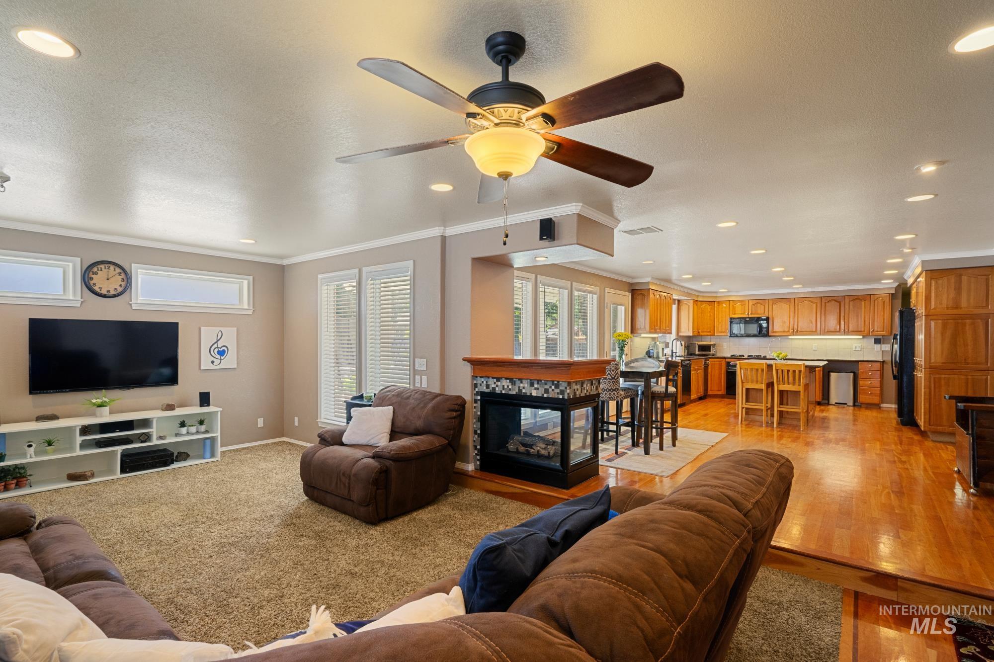 Living room featuring recessed lighting, a multi sided fireplace, a ceiling fan, and crown molding