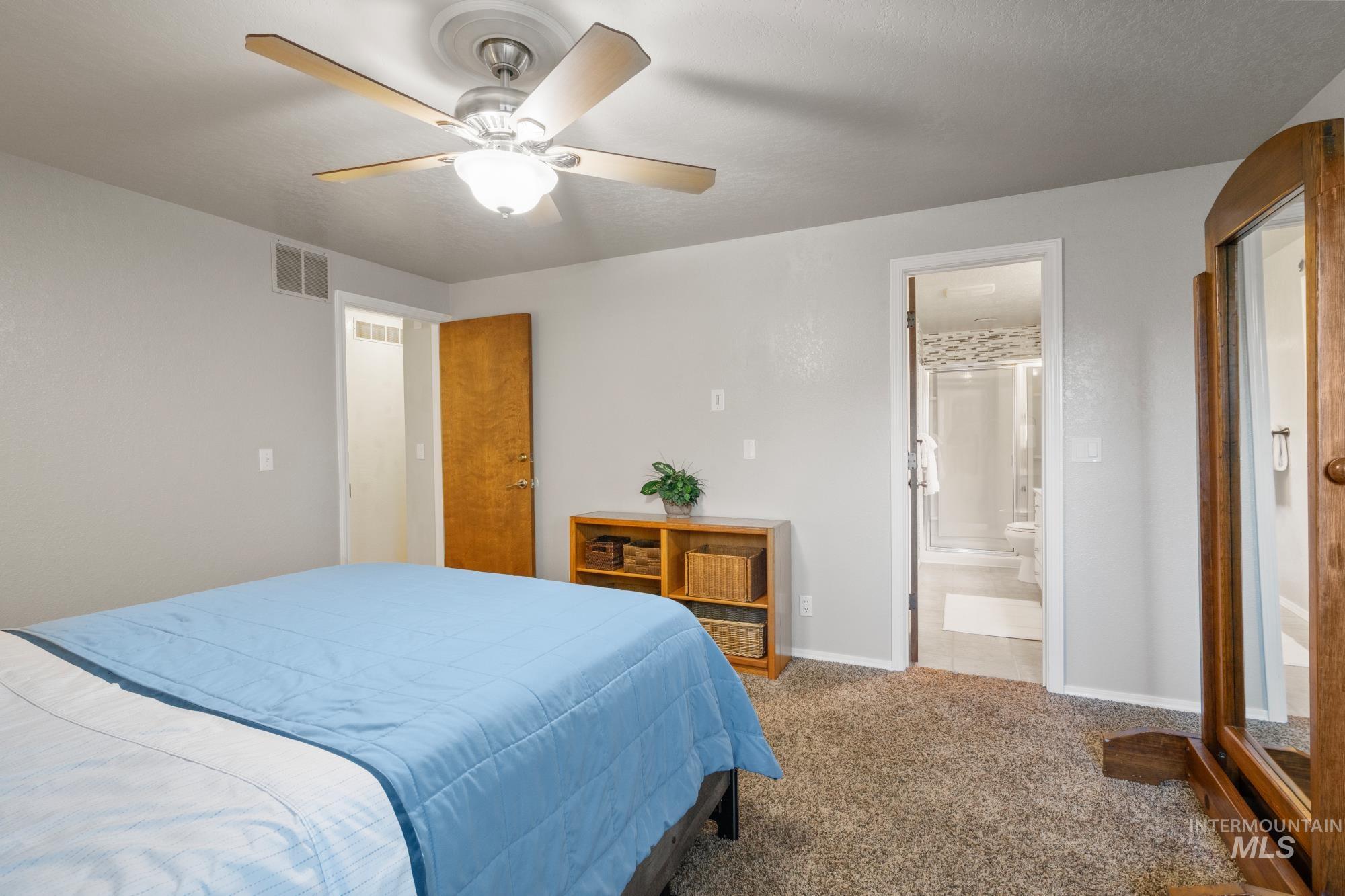 Carpeted bedroom with ensuite bath and ceiling fan