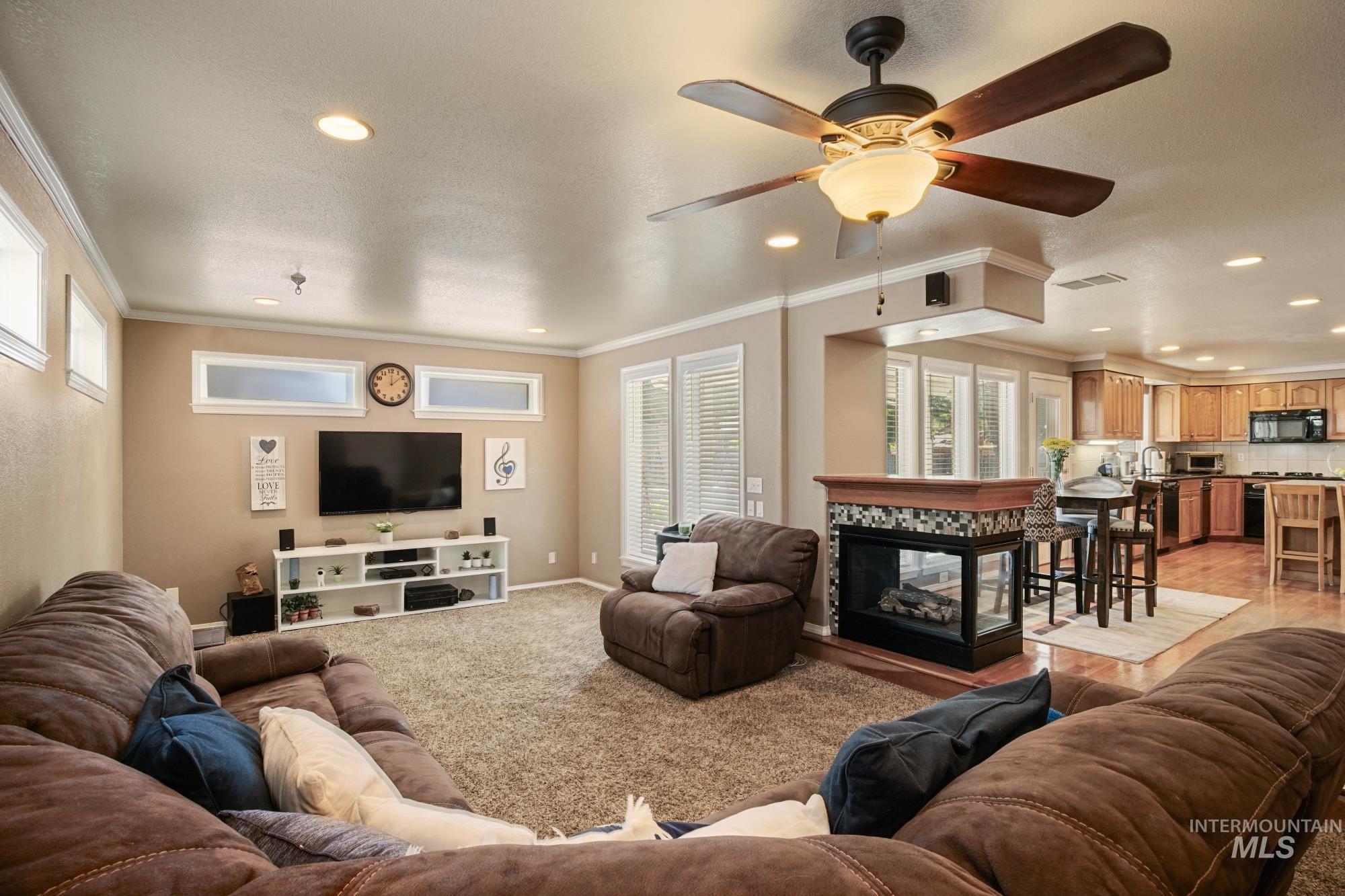Living area with ornamental molding, light carpet, recessed lighting, a ceiling fan, and a multi sided fireplace