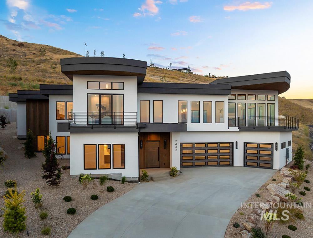 Rear view of house featuring an attached garage, stucco siding, concrete driveway, and a balcony