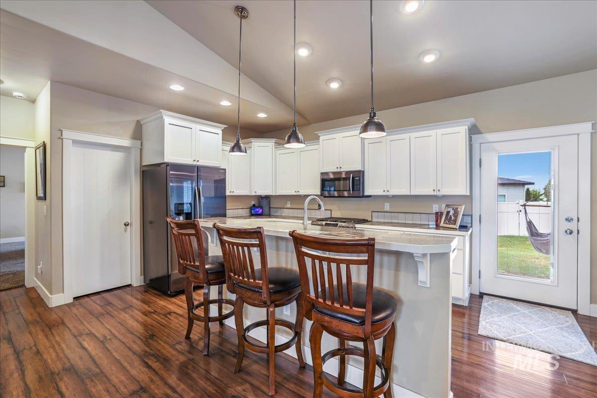 Kitchen with appliances with stainless steel finishes, lofted ceiling, dark wood-style flooring, light countertops, and white cabinets