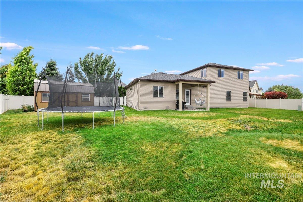 Rear view of property with a trampoline, a fenced backyard, and a storage shed