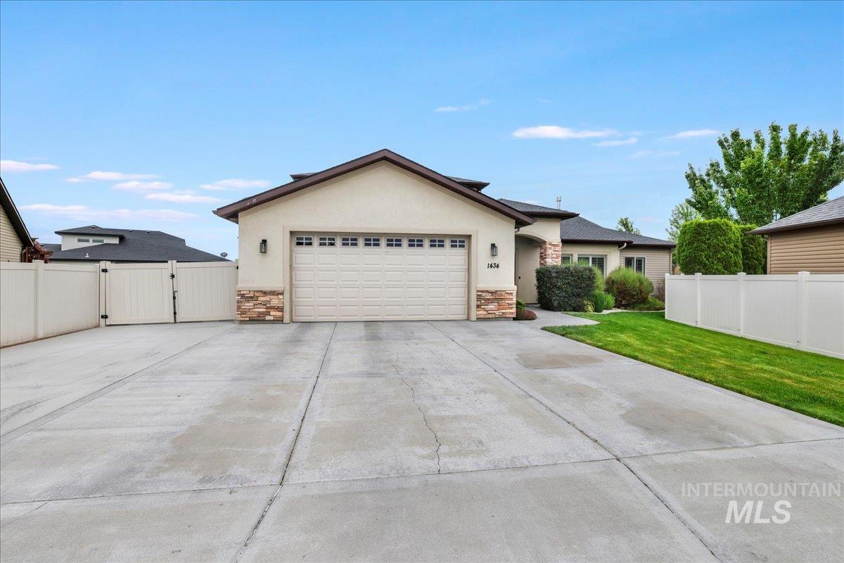 Single story home featuring stone siding, a gate, concrete driveway, an attached garage, and stucco siding