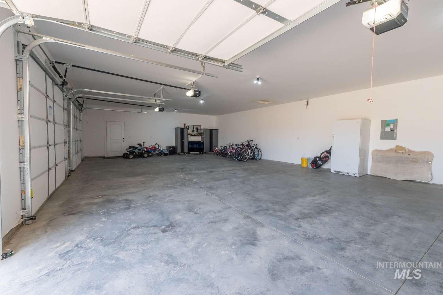 Garage with a garage door opener, freestanding refrigerator, and electric panel