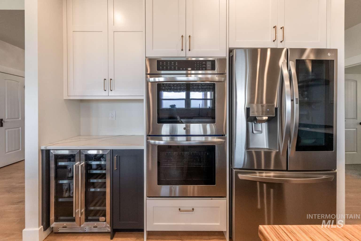 Kitchen with stainless steel appliances, white cabinetry, wine cooler, light wood-style flooring, and light stone countertops