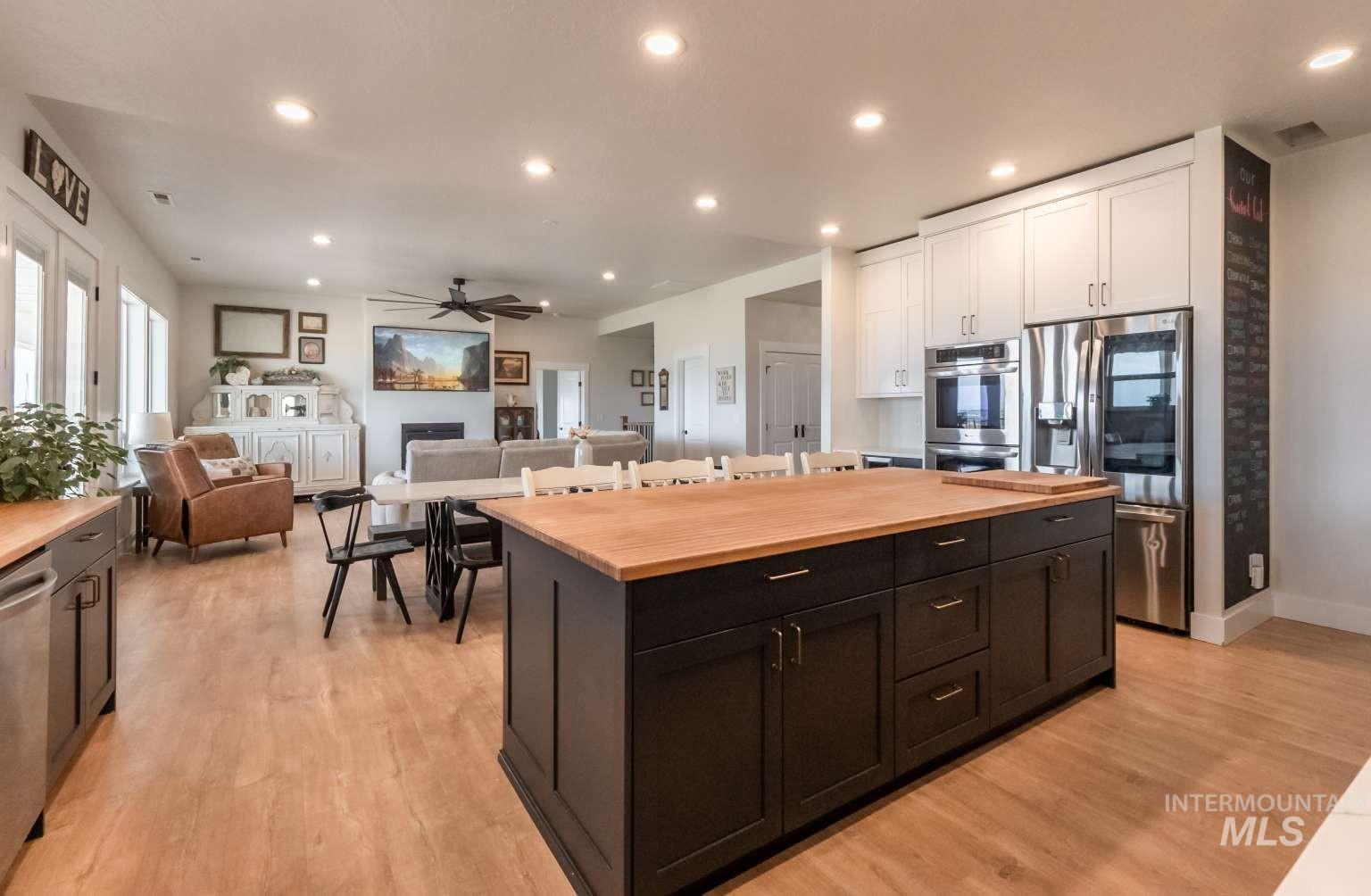 Kitchen with recessed lighting, stainless steel appliances, dark cabinetry, open floor plan, and light wood finished floors