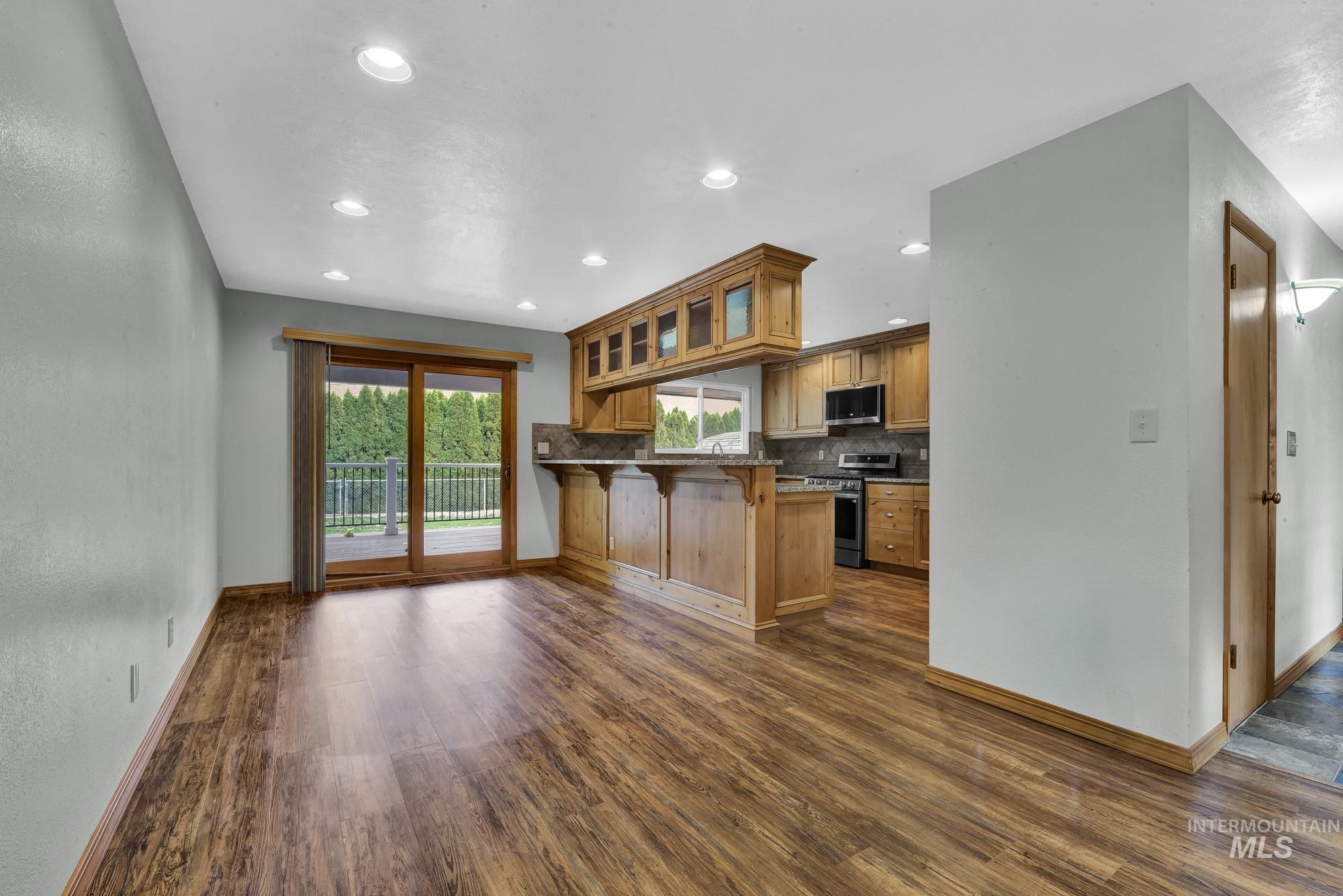 Kitchen featuring glass insert cabinets, a breakfast bar, tasteful backsplash, appliances with stainless steel finishes, and dark wood-style floors