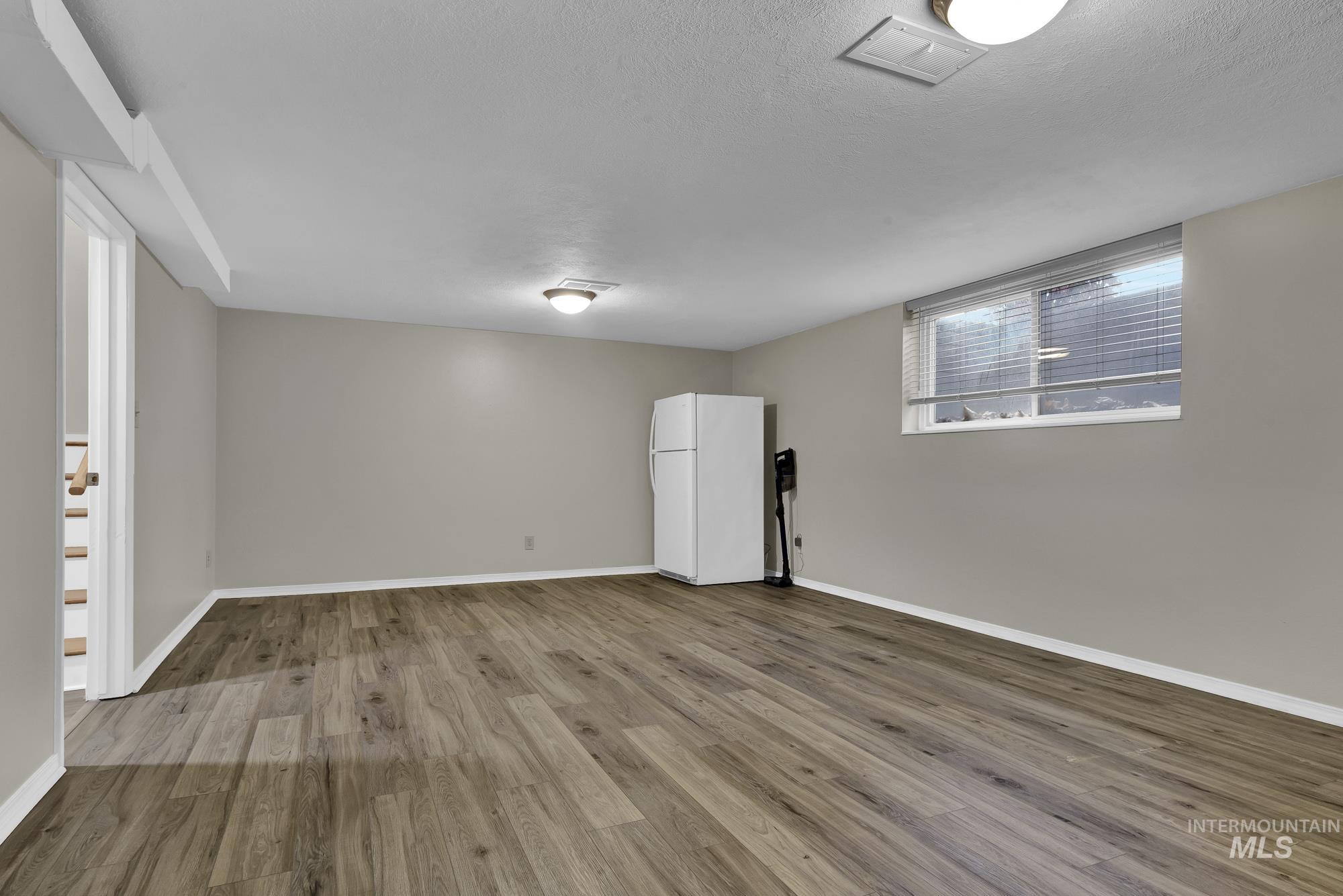 Unfurnished room with wood finished floors, a textured ceiling, and stairs