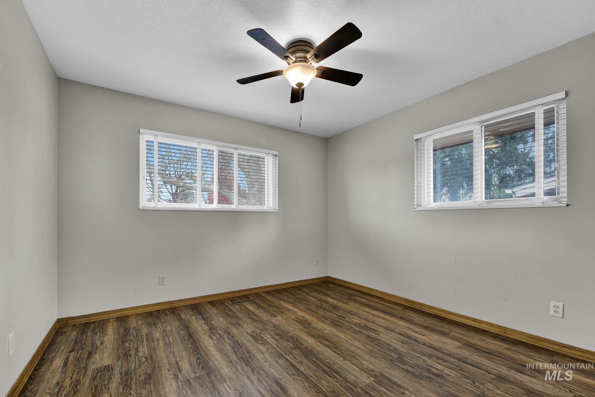 Empty room with dark wood-type flooring, healthy amount of natural light, and a ceiling fan