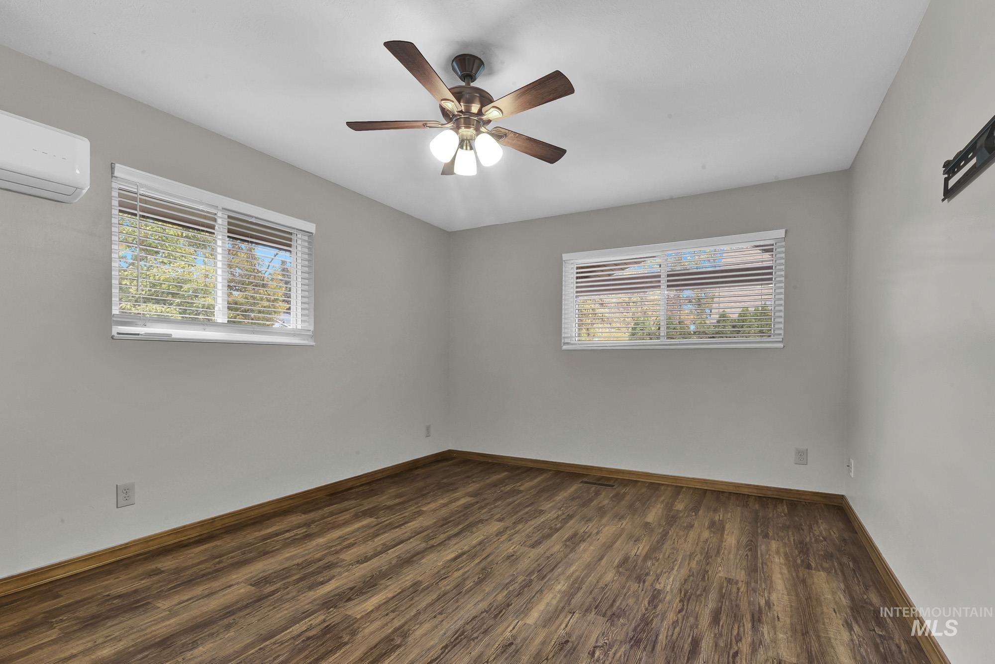 Empty room featuring dark wood-type flooring, ceiling fan, and a wall unit AC