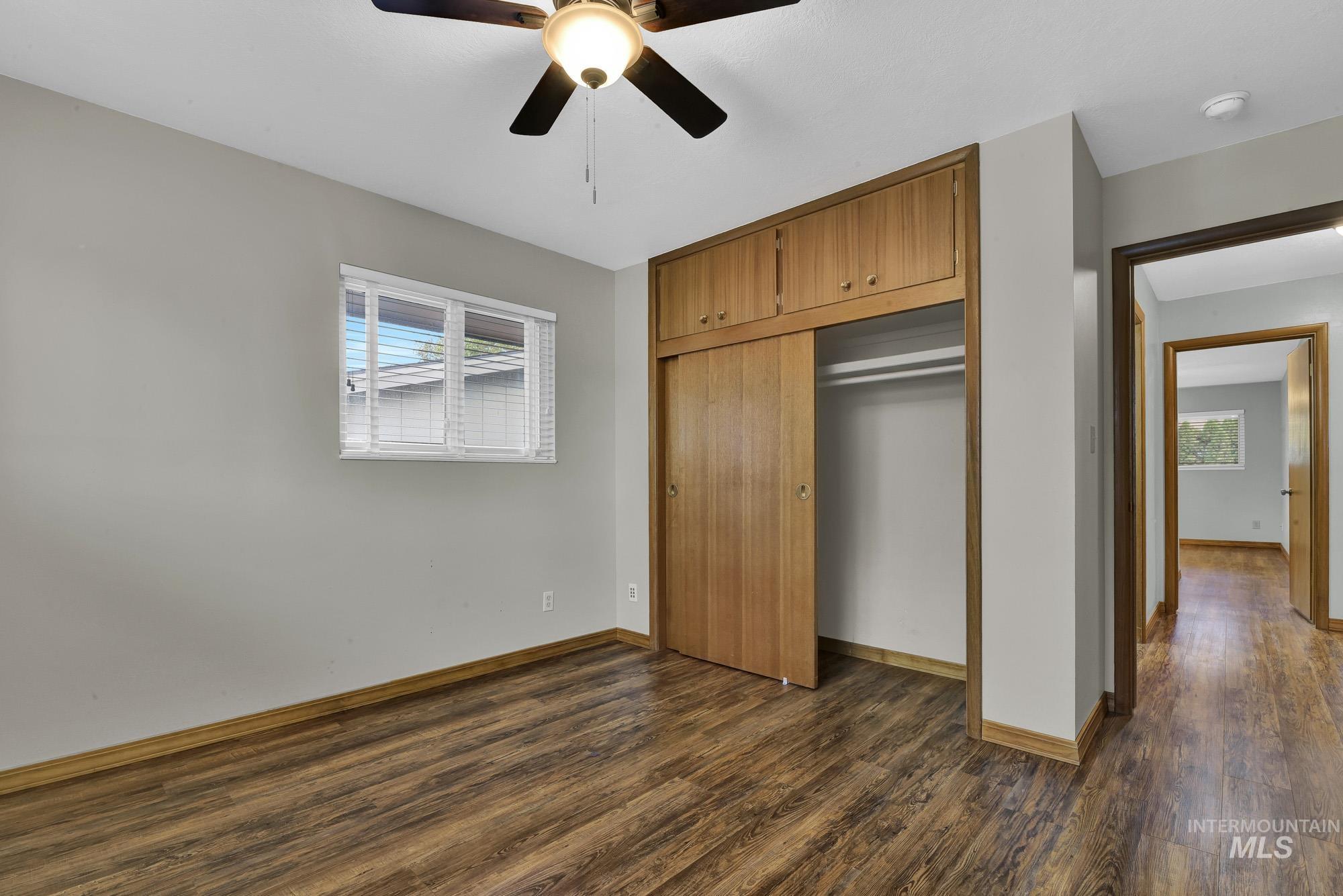 Unfurnished bedroom featuring dark wood-style floors, multiple windows, and ceiling fan