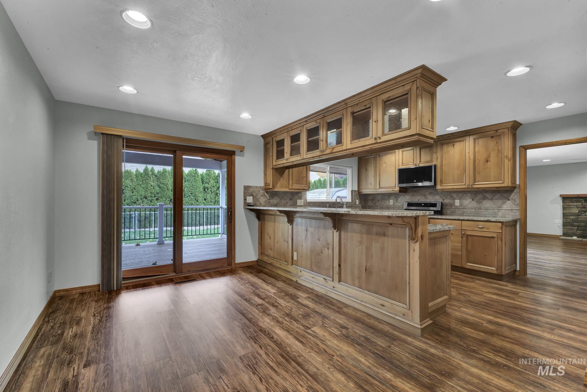 Kitchen with glass insert cabinets, backsplash, dark wood finished floors, a kitchen bar, and a peninsula