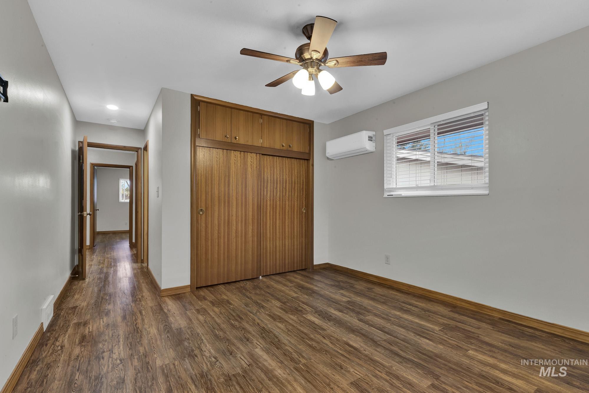 Unfurnished bedroom with dark wood-type flooring, a ceiling fan, a closet, and a wall unit AC