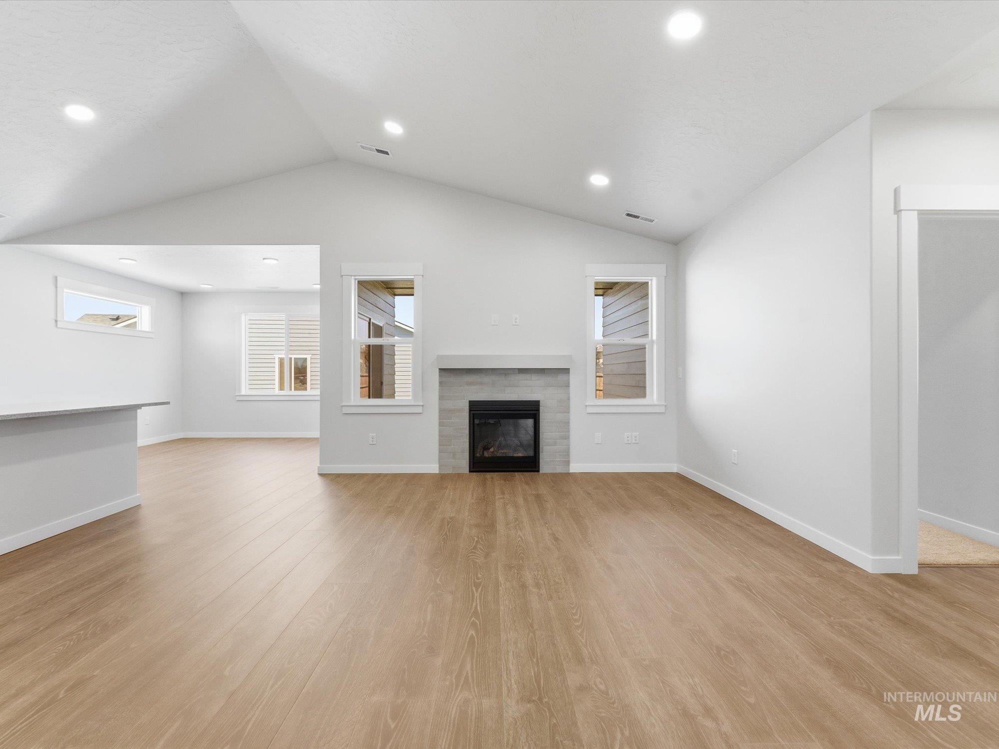 Living area featuring a vaulted ceiling with recessed lighting, wood-finish flooring, and a fireplace with a light gray mantel