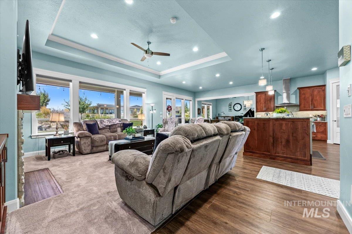 Living room with a ceiling fan, a tray ceiling, dark wood-style flooring, and recessed lighting