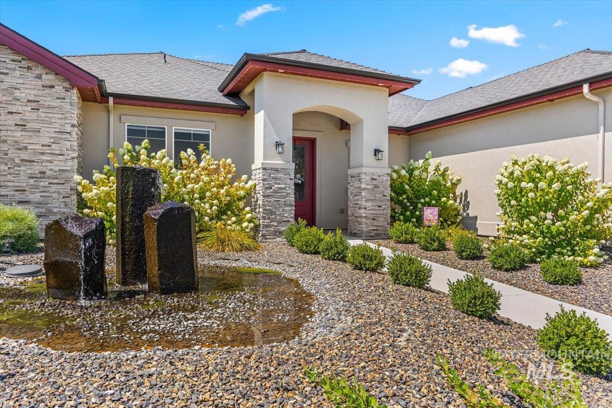 Doorway to property featuring stone siding, stucco siding, and a shingled roof