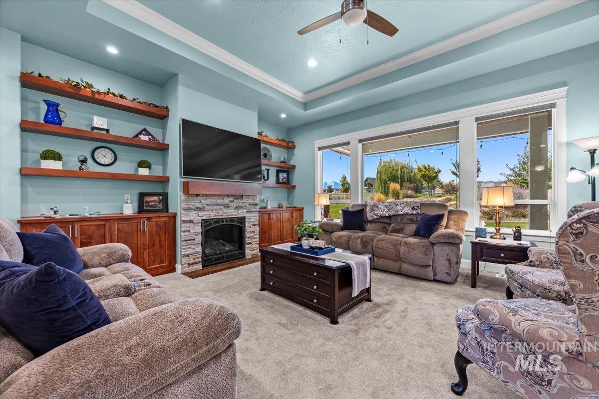 Living area with a tray ceiling, light colored carpet, a stone fireplace, built in shelves, and recessed lighting