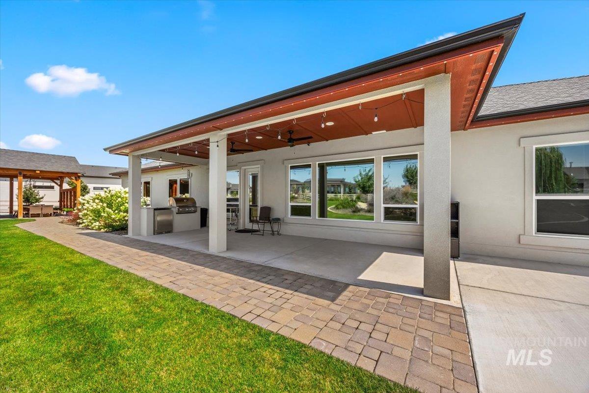 Rear view of property with an outdoor kitchen, a patio, stucco siding, a yard, and a ceiling fan
