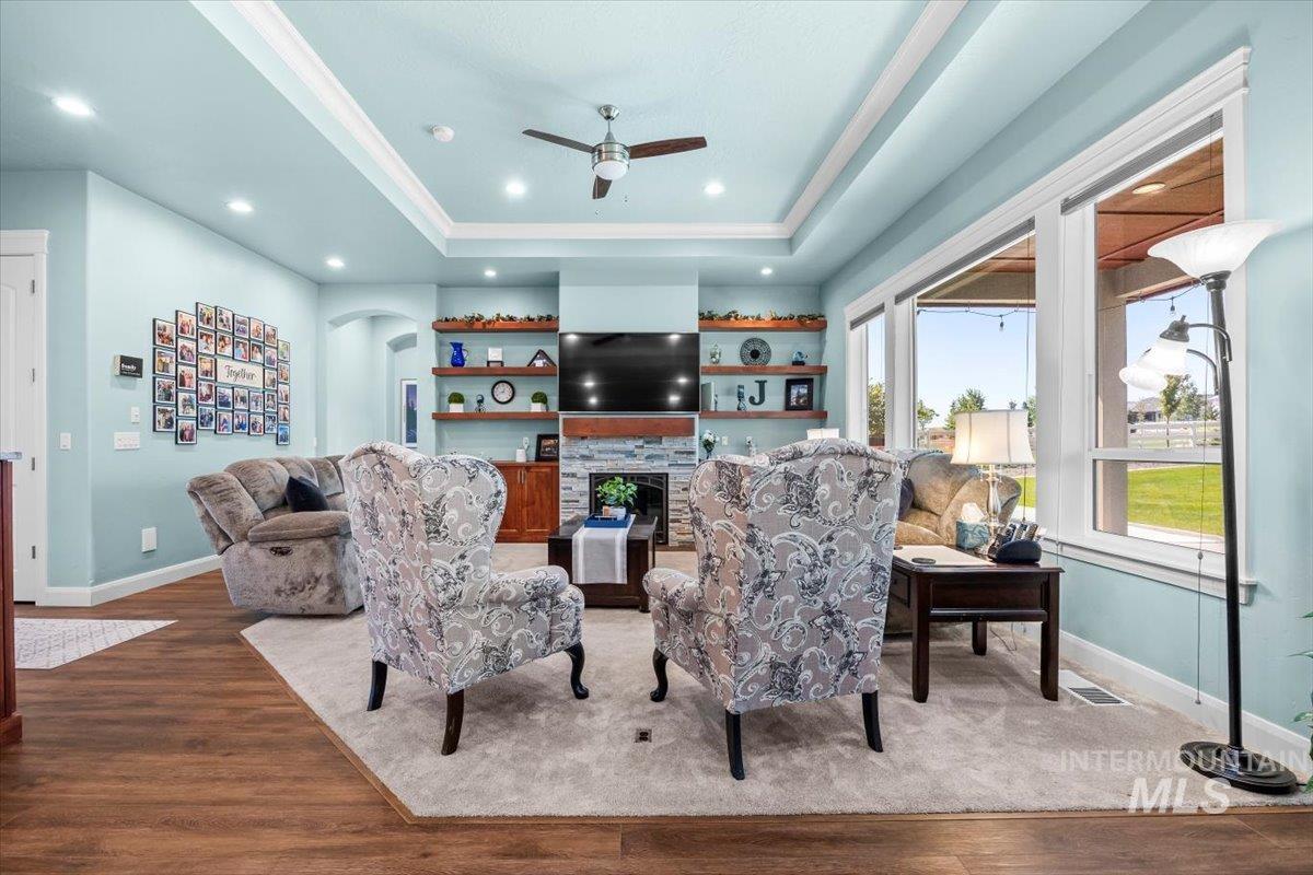 Living area featuring a tray ceiling, wood finished floors, arched walkways, a fireplace, and recessed lighting