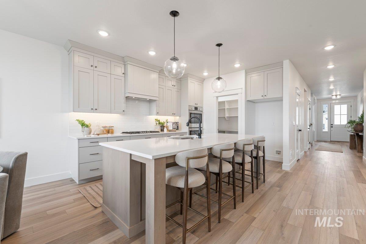 Kitchen featuring a kitchen bar, white cabinets, light wood-type flooring, a kitchen island with sink, and decorative backsplash