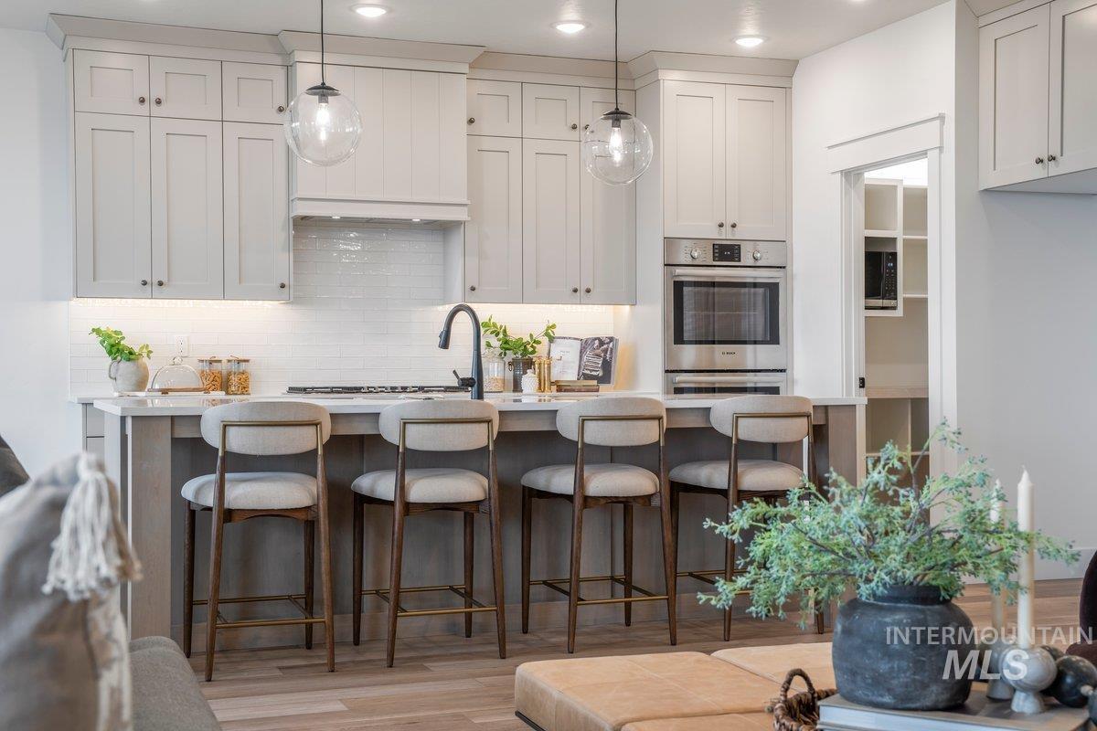 Kitchen featuring backsplash, light wood-style flooring, white cabinetry, a breakfast bar area, and pendant lighting